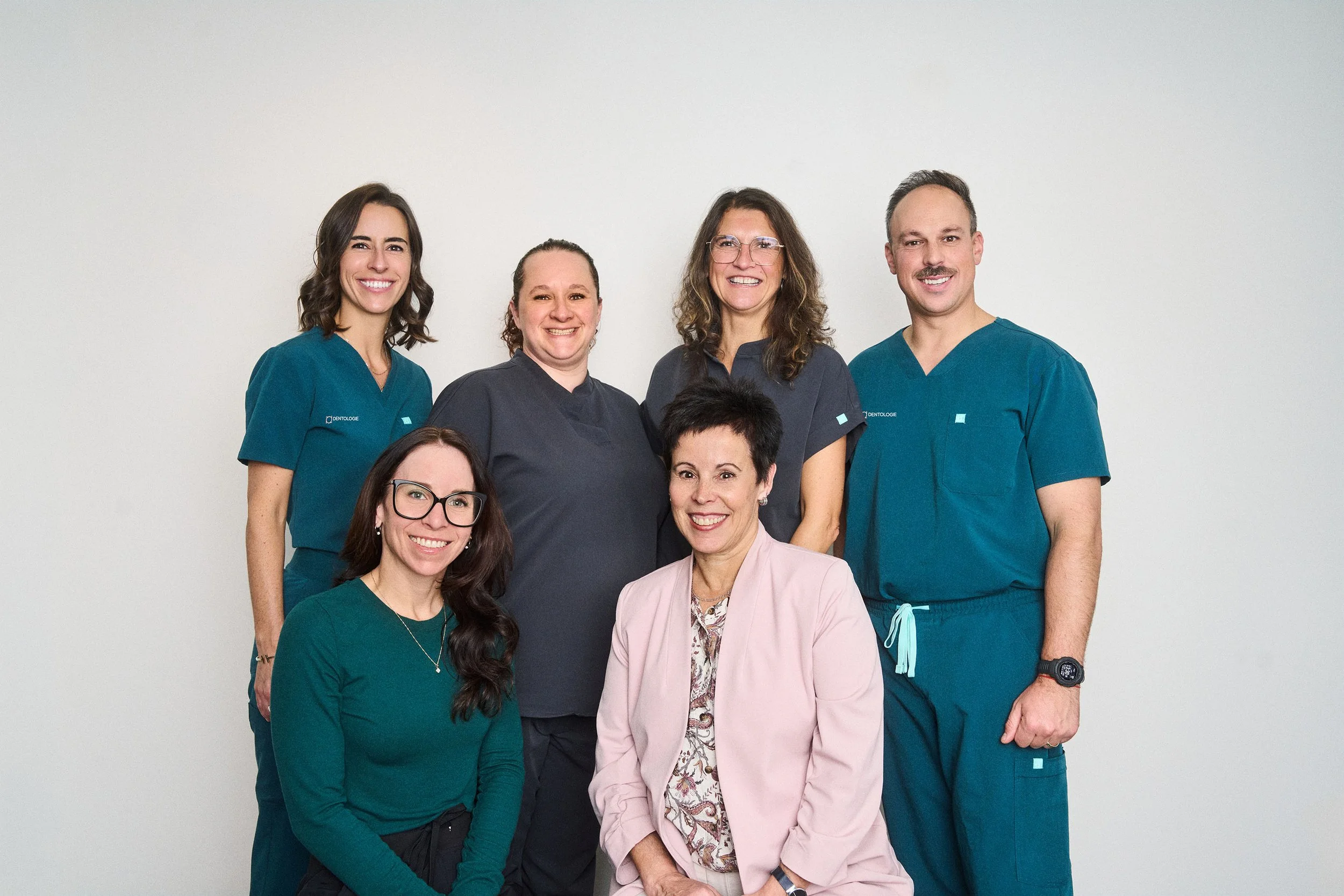 Photo de groupe d’une équipe de clinique dentaire souriante, composée de six femmes et d’un homme en tenue médicale.