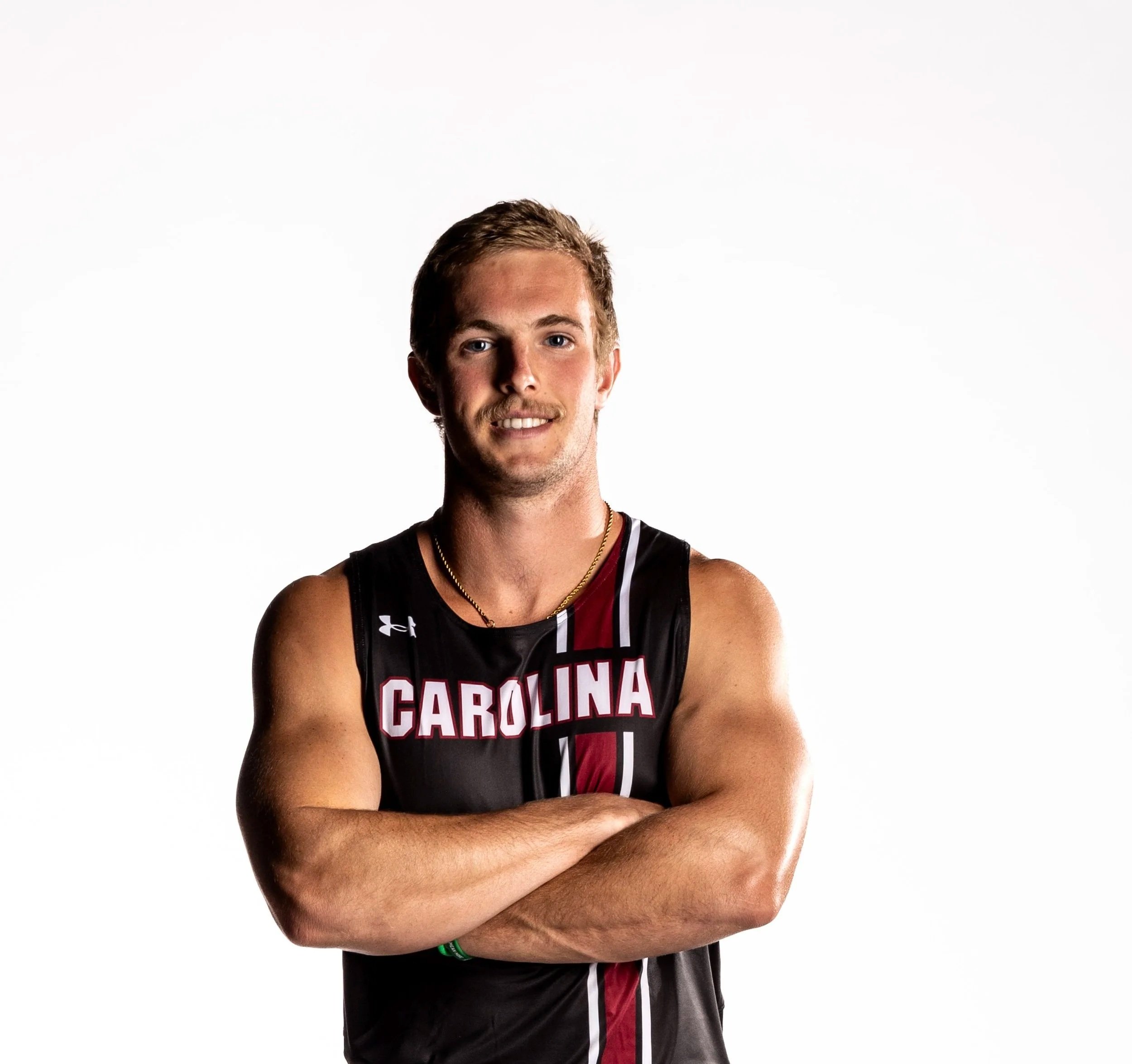 A young male athlete wearing a black university basketball jersey with red and white accents, standing with his arms crossed in front of a plain white background.