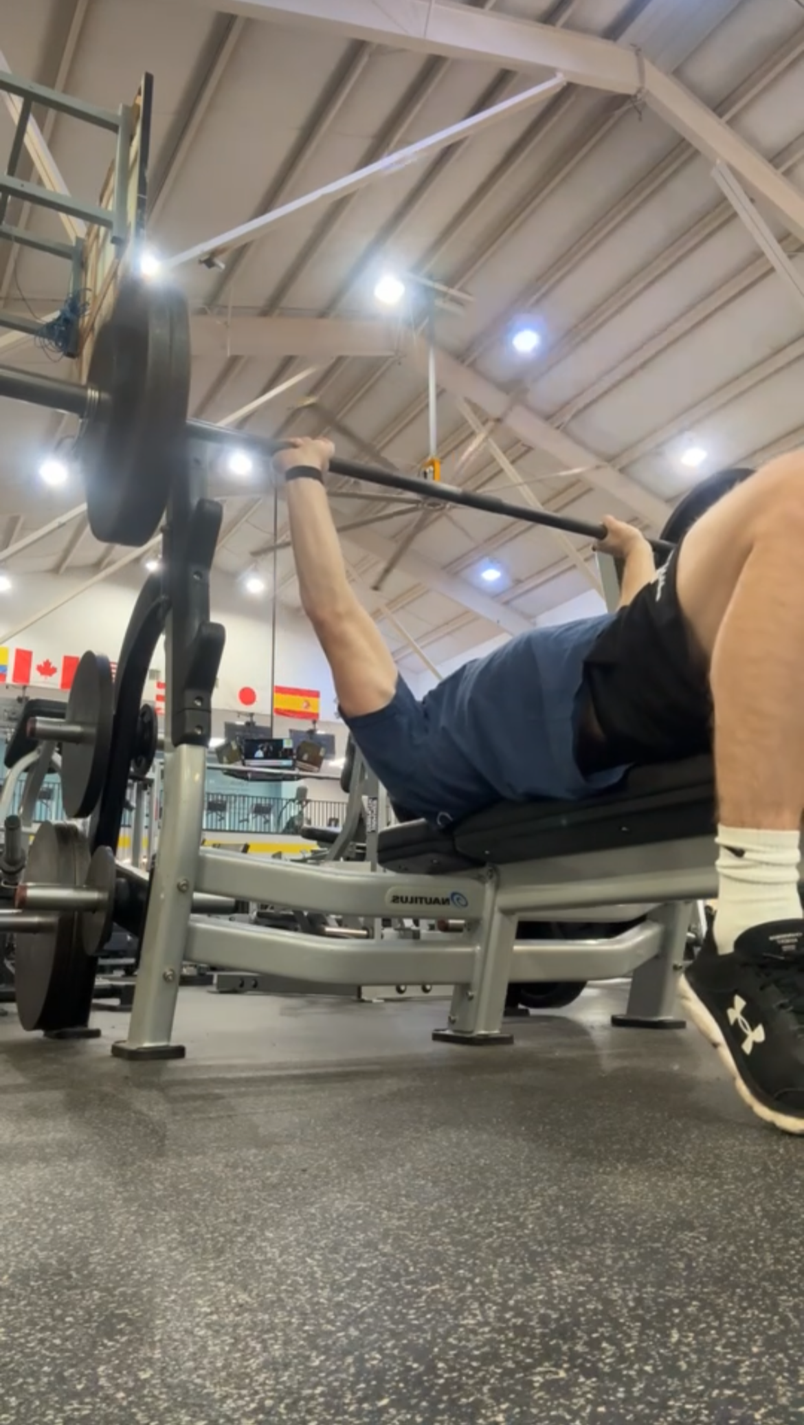 A person in a gym lying on a bench press machine, lifting a barbell.