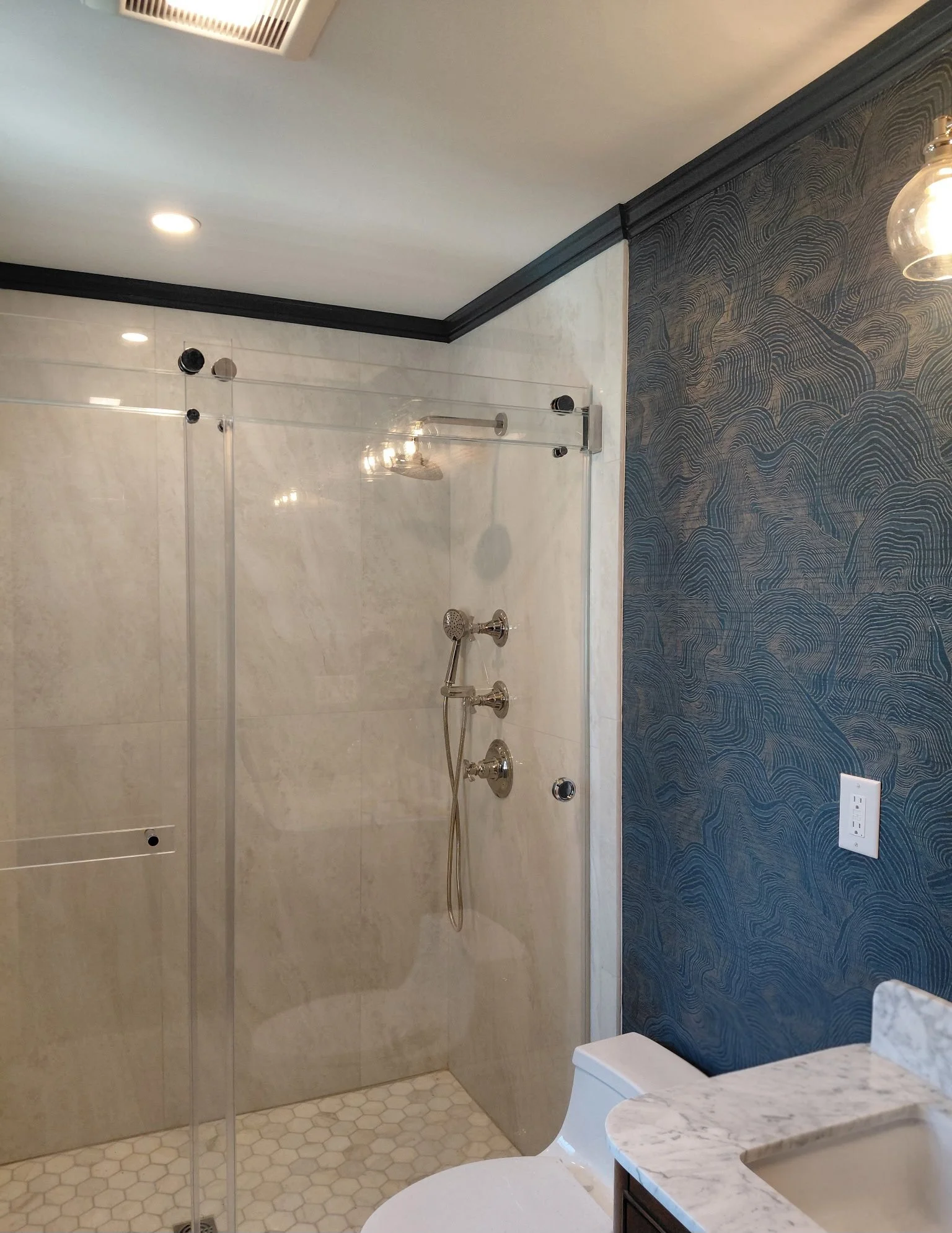 Modern bathroom with a walk-in shower, hexagonal tile floor, marble countertop, and a dark textured accent wall.