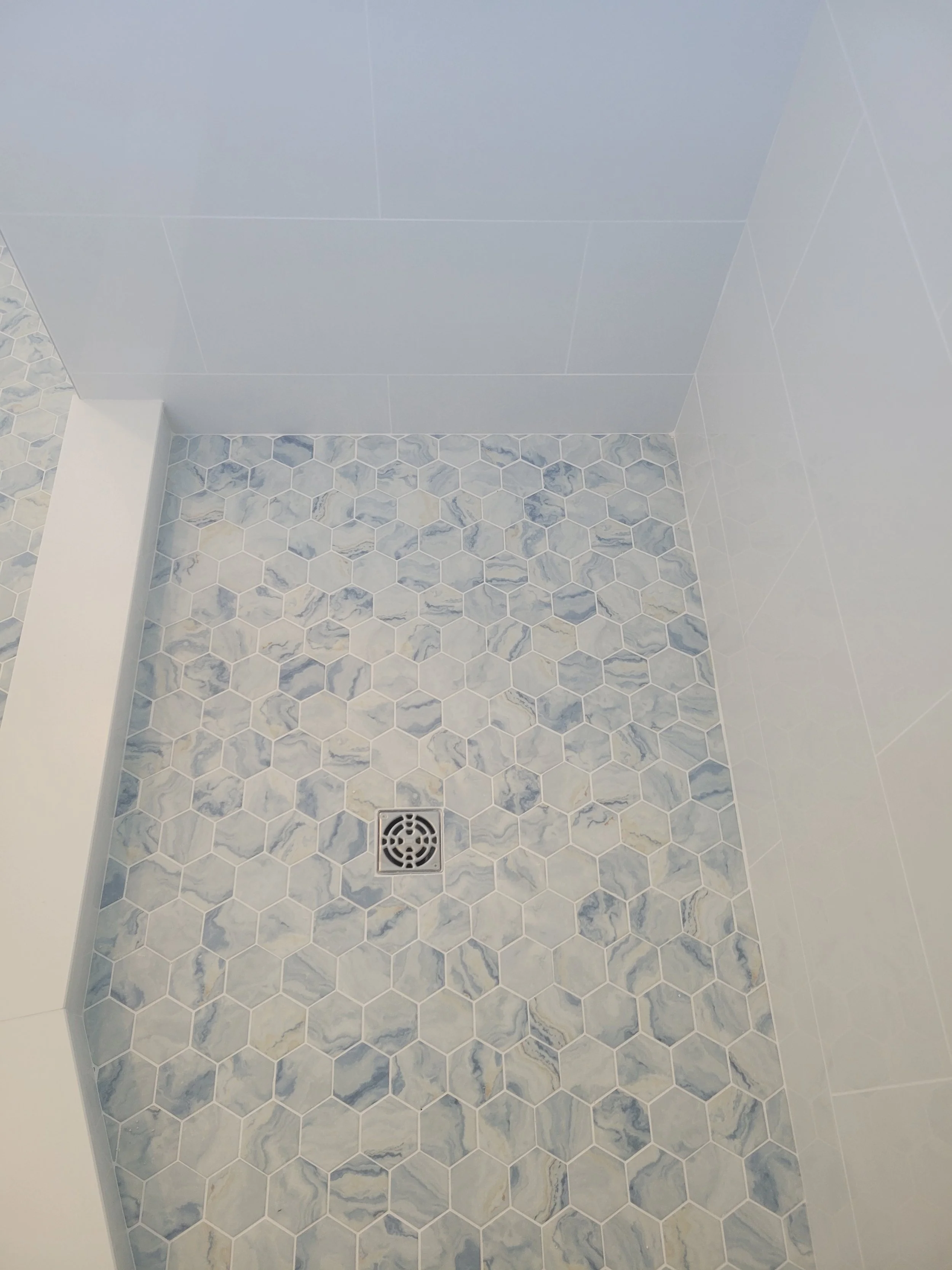 Shower area with hexagon marble tiles on the wall and floor, drain in the center, and a white ceiling.