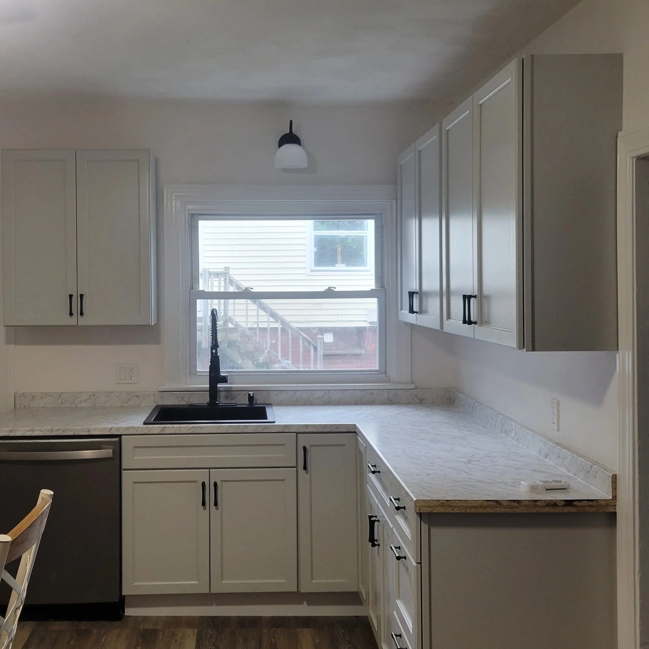 Kitchen with white cabinets, a granite countertop, and a large window above the sink, with a black faucet.