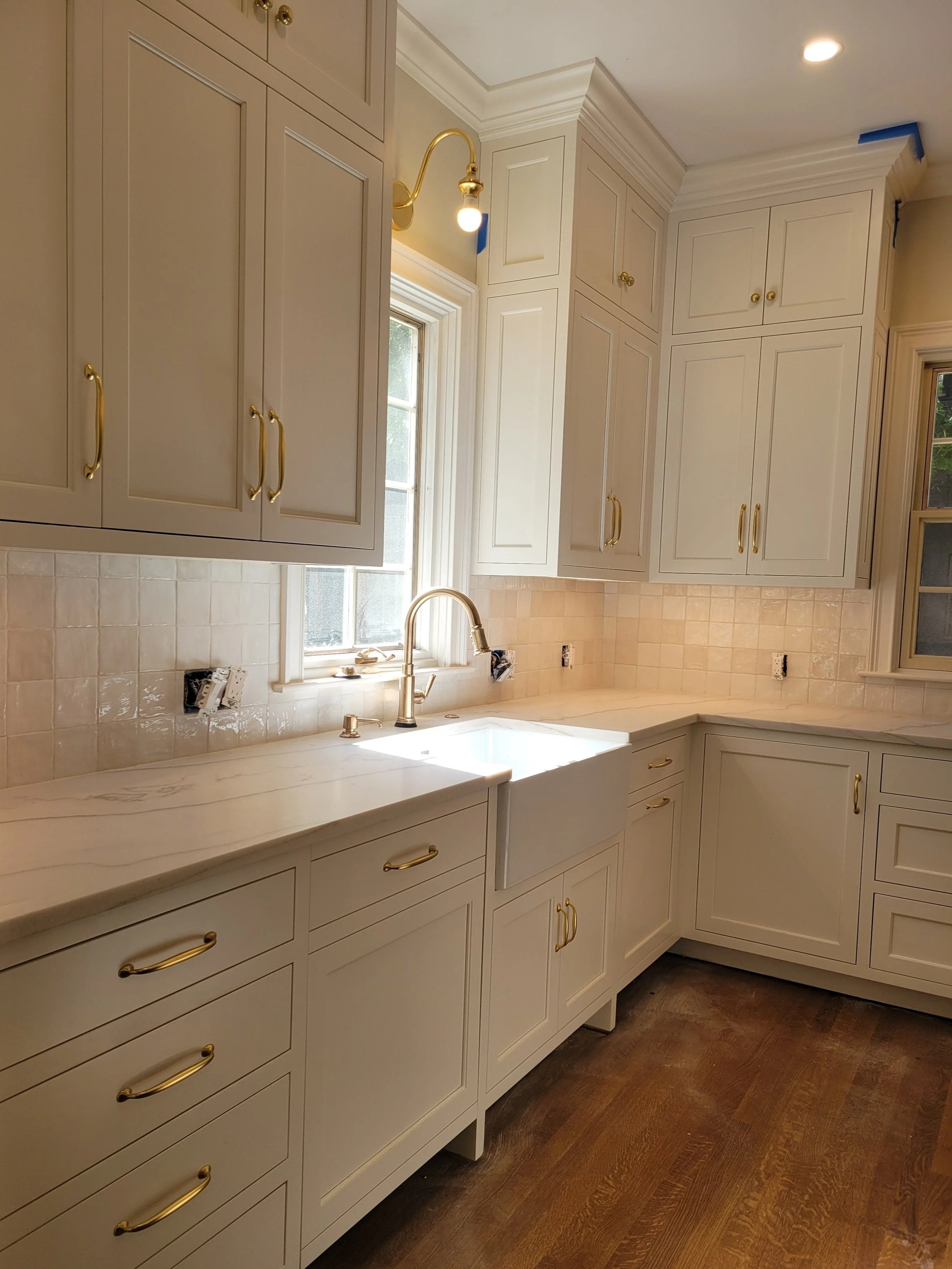 Kitchen with white cabinets, gold handles, a window, and a gold faucet over a white sink.