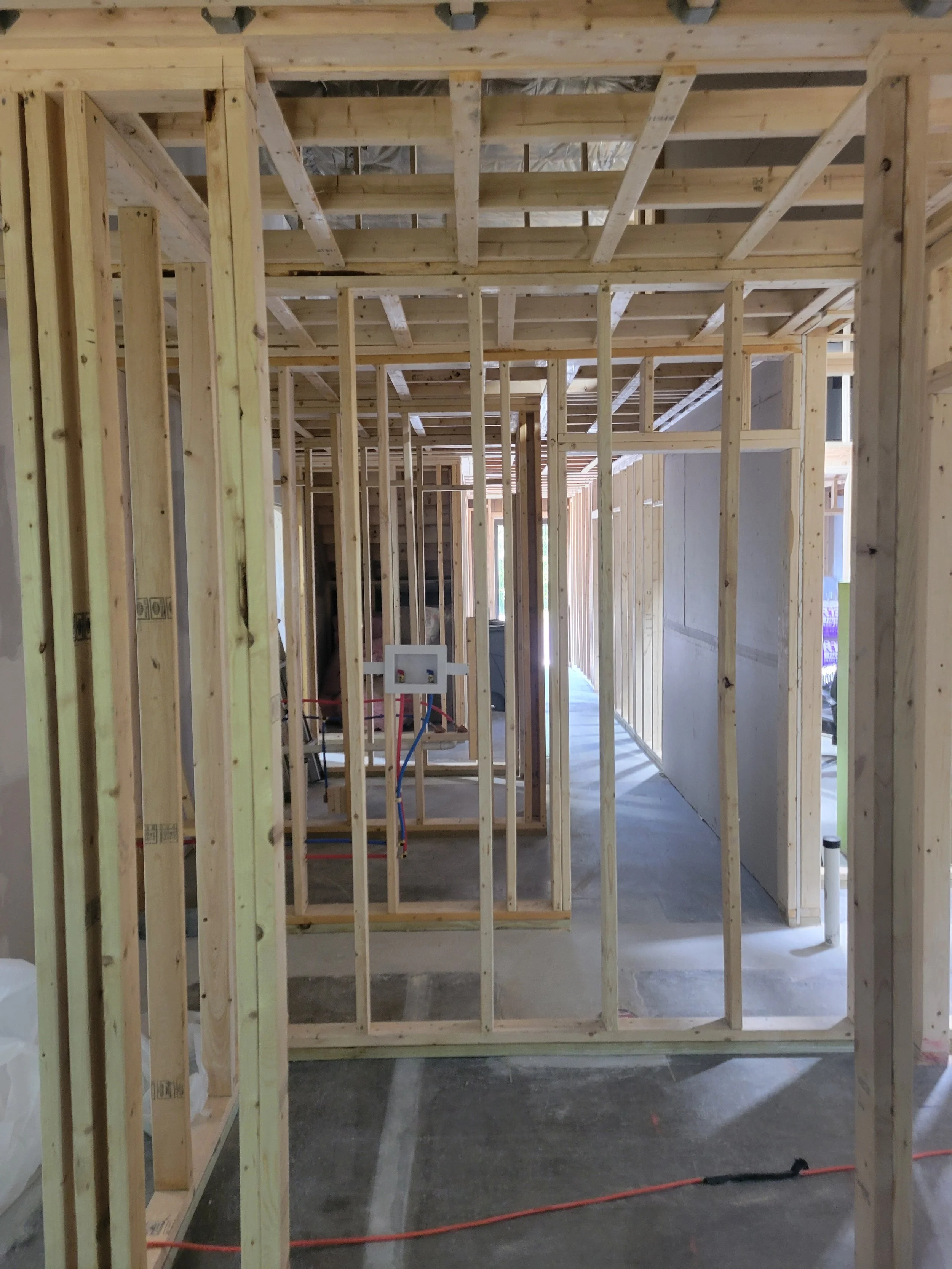 Interior view of a construction site with exposed wooden framing for walls and ceiling, with some electrical wiring visible on the floor.