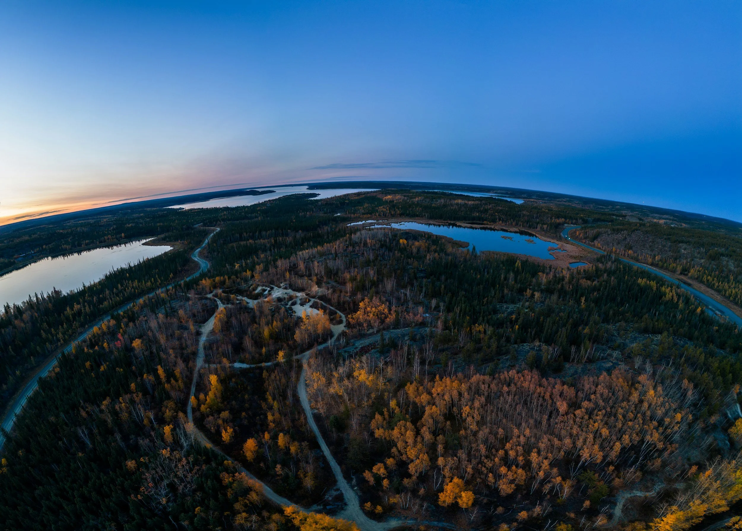 Aerial view of a landscape at dusk with lakes, forests, and winding roads.