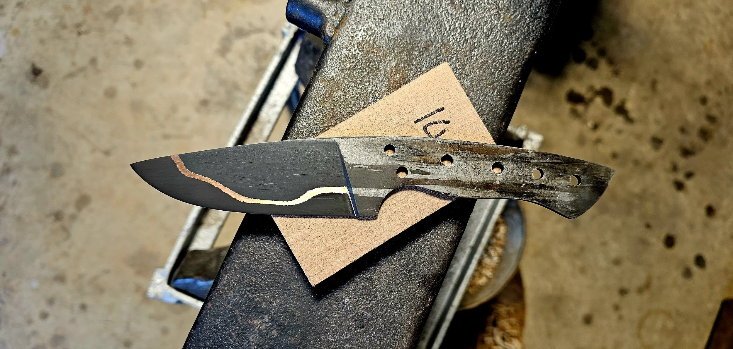 A partially finished knife with a black blade, resting on a workbench in a workshop.