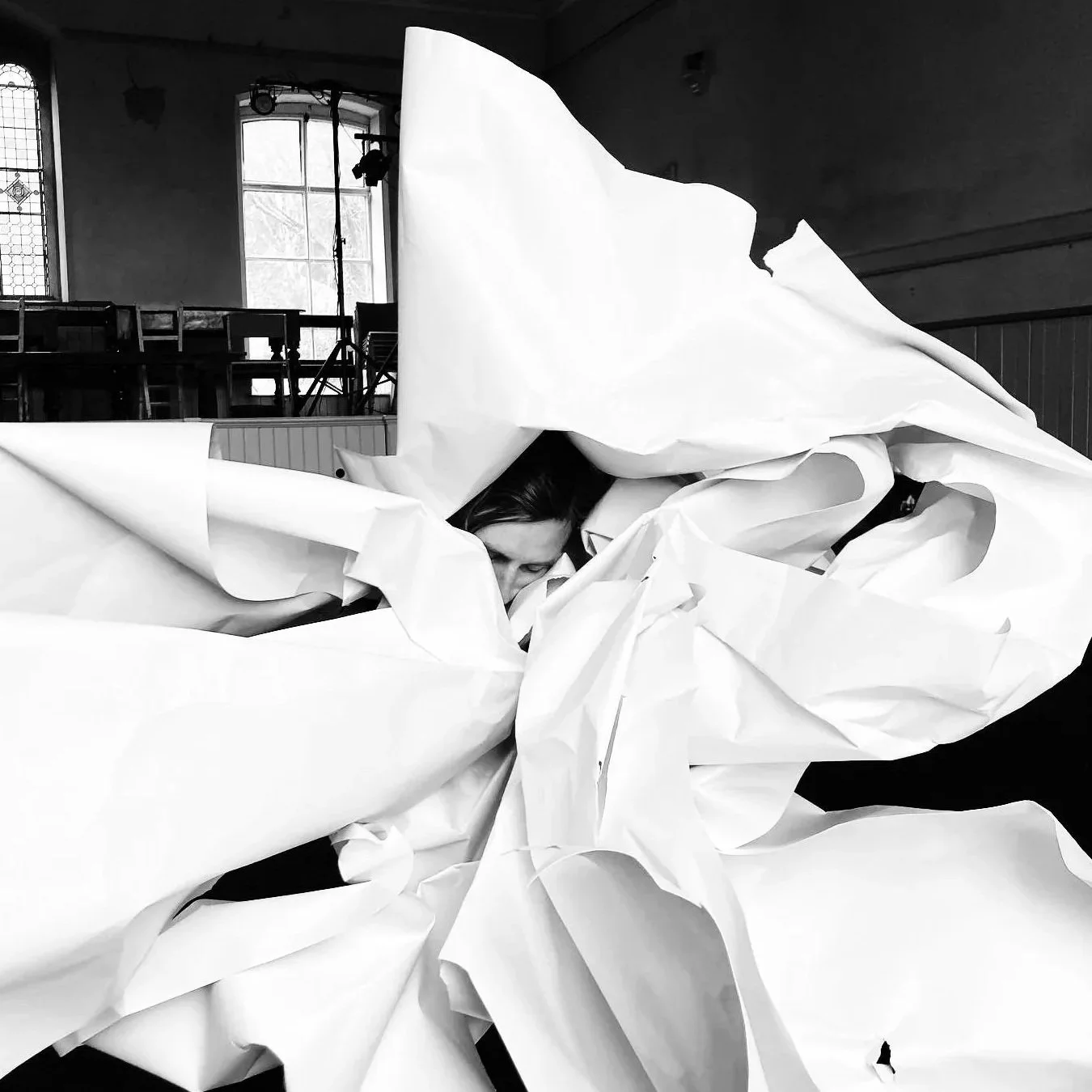 A person - partially hidden or wrapped by large crumpled white sheets of paper...as if becoming a flower or sea creature