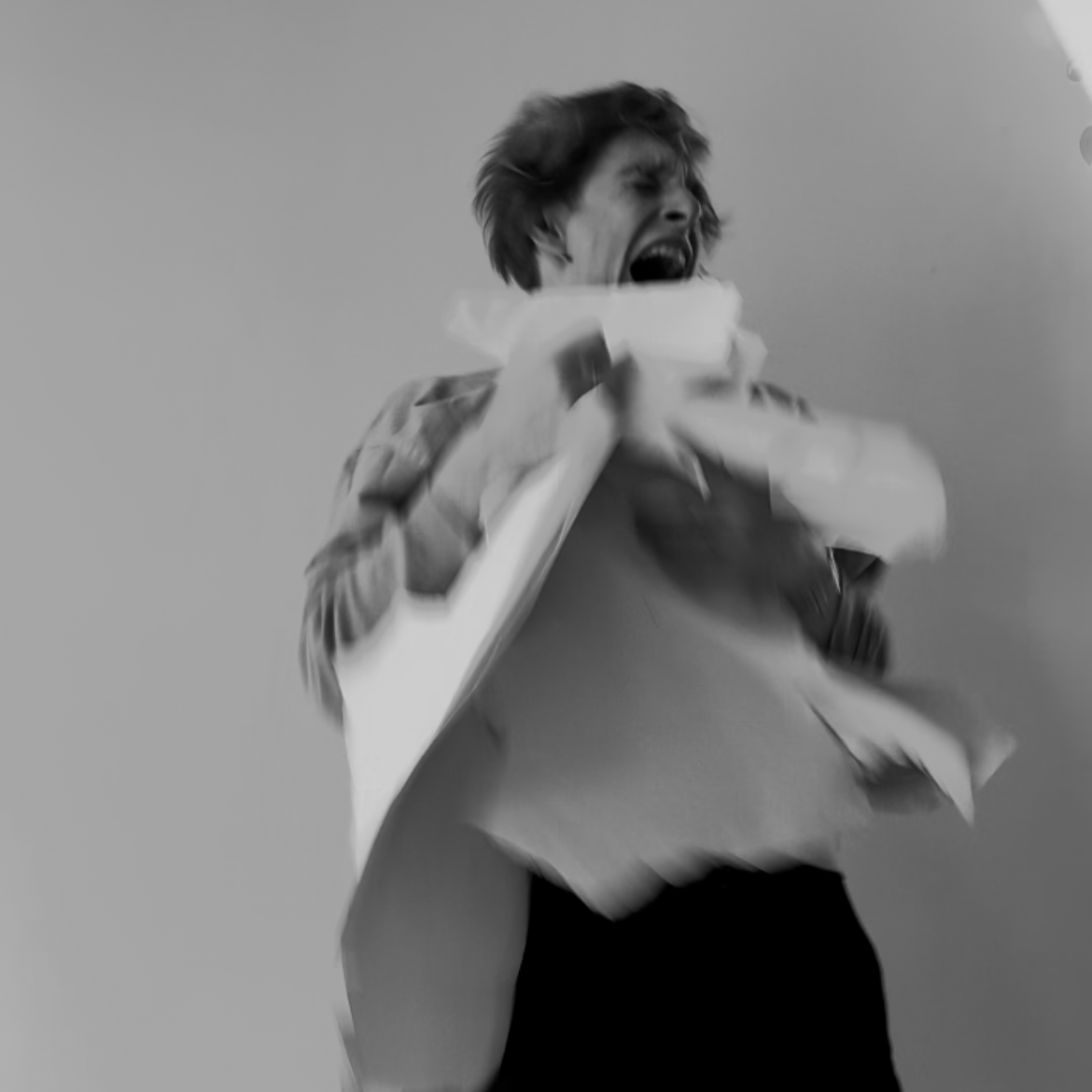 A person with short hair wearing a jacket, captured in a black-and-white photo, appears to be screaming or shouting while clutching a stack of papers.