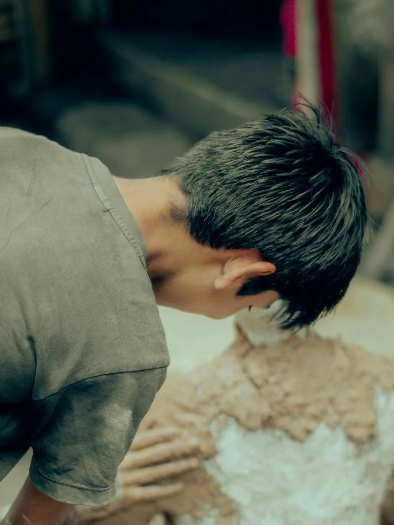 A person with short gray hair creating something out of clay with bare hands