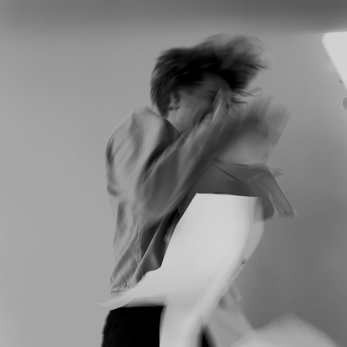 Blurred black and white photo of a person with long hair caught in motion, seemingly working with paper, with a plain background.