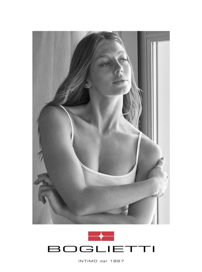 Black and white portrait of a woman with long hair standing by a window with natural light