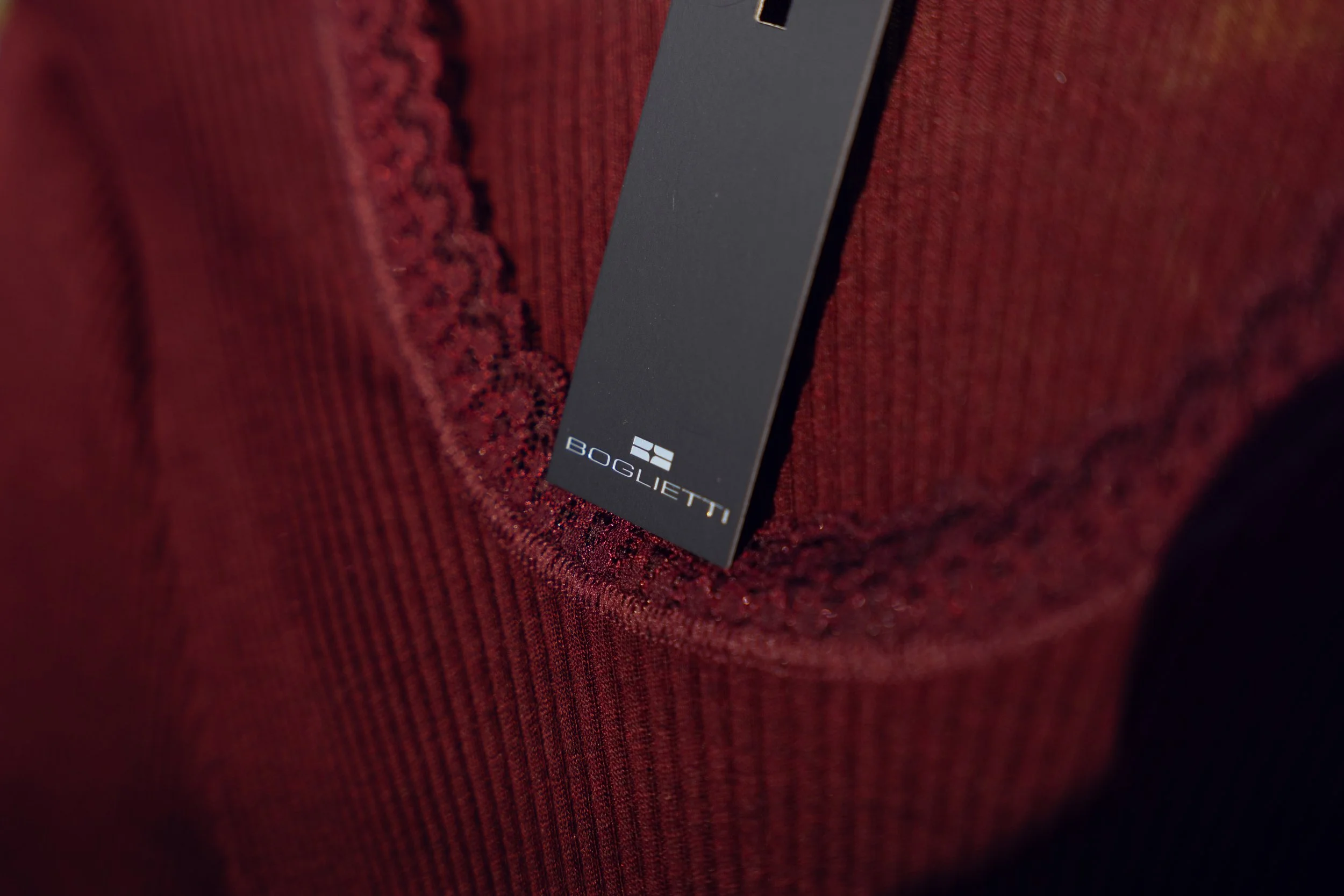 Close-up of a black clothing tag labeled 'BOGLIETTI' attached to red fabric with embroidered accents.