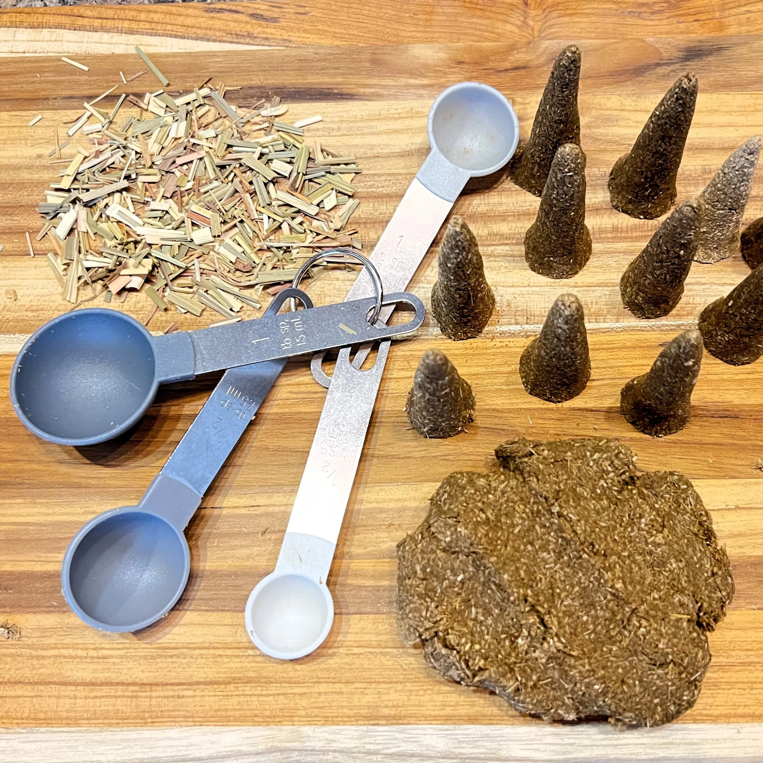 A wooden table holds several objects including loose small wood pieces, a plastic measuring scoop, and multiple incense cones.