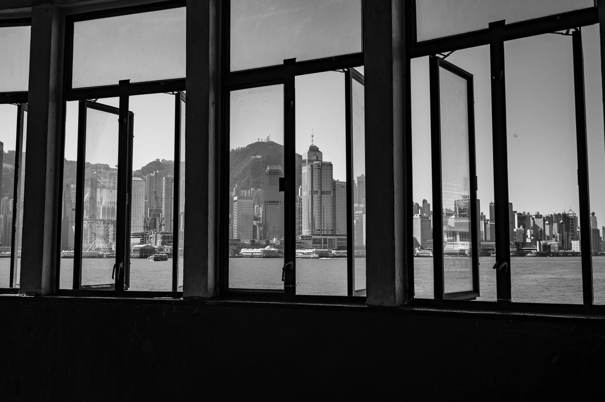 Black-and-white photo of a city skyline viewed through windows of a building, with mountains in the background.