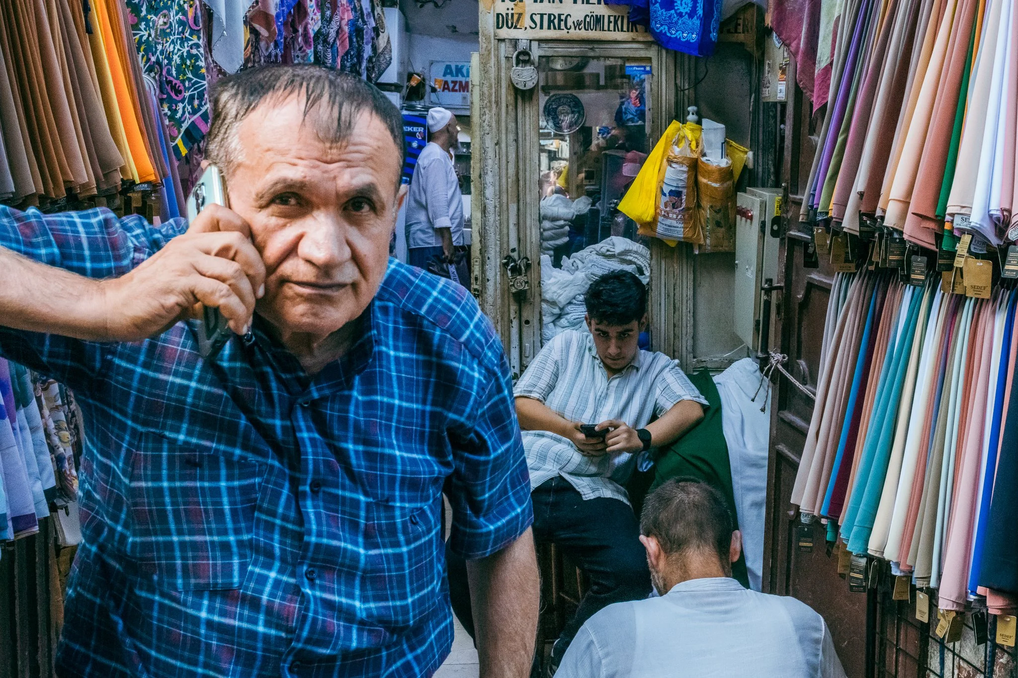 Group of men shopping in a fabric or clothing store with shelves of colorful fabrics and textiles around them.