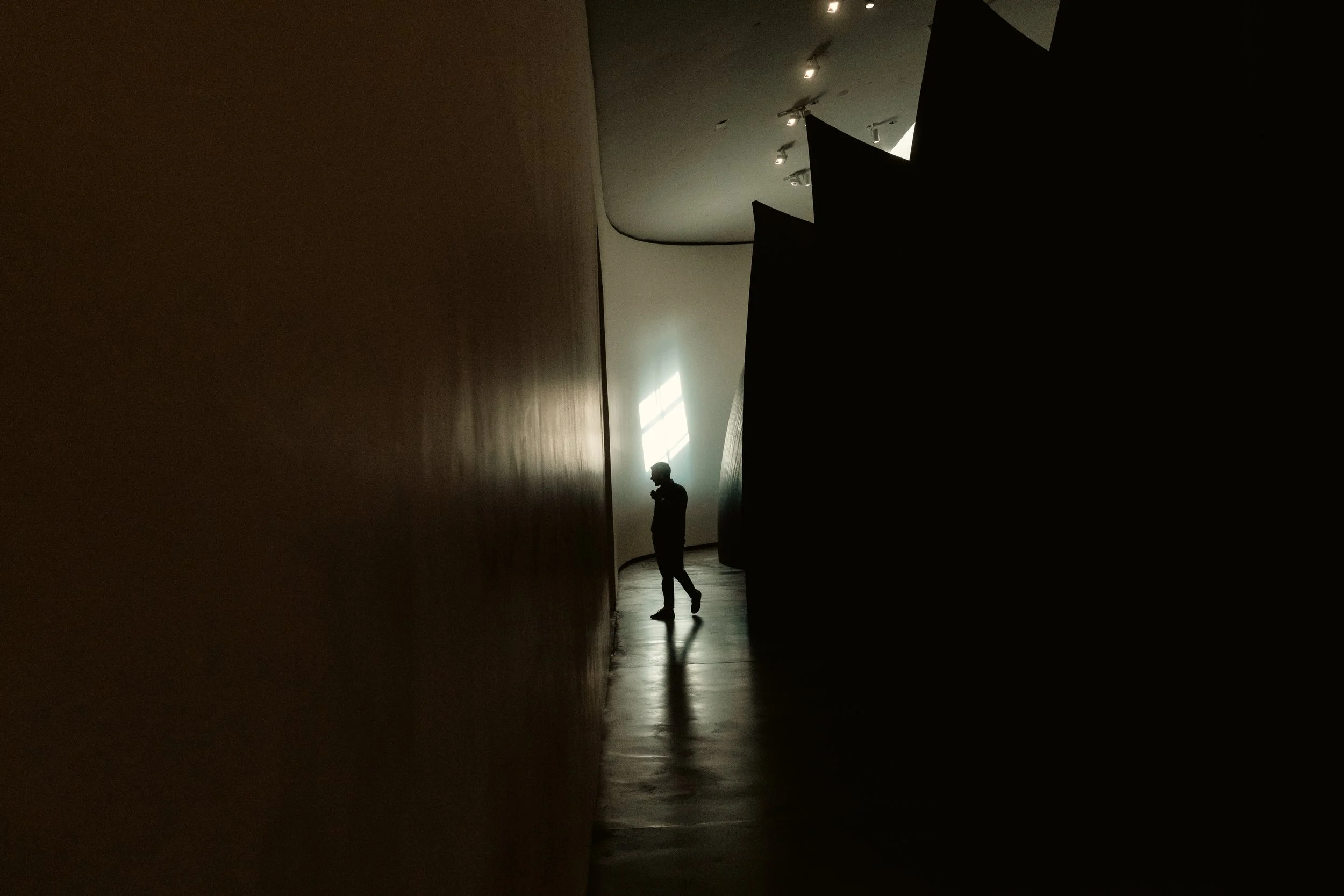 Silhouette of a person standing in a dimly lit hallway with a large window allowing natural light in.