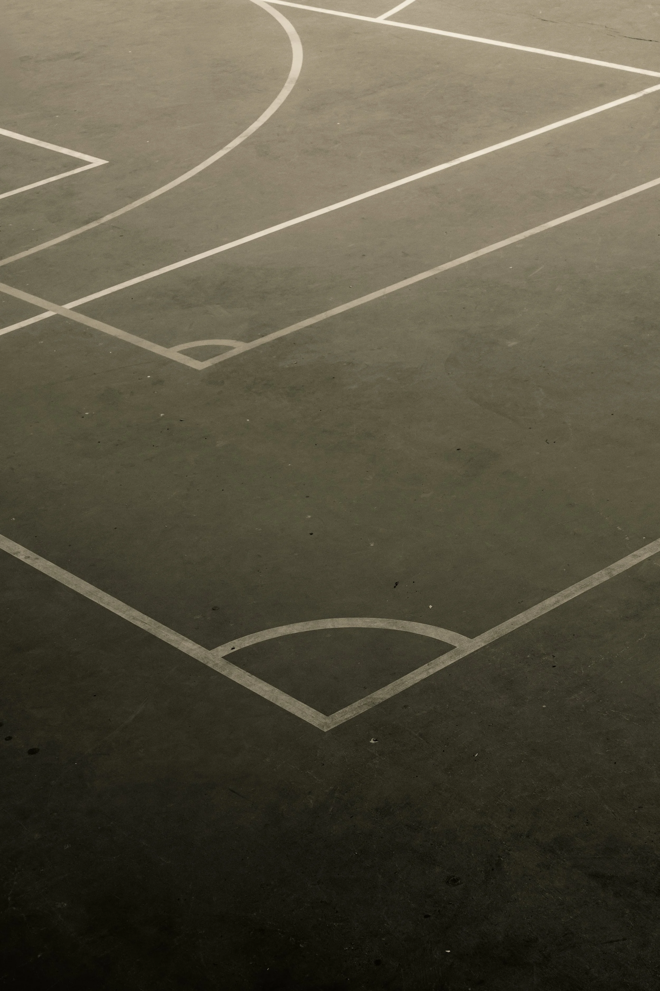 Empty basketball court with visible white court lines on a concrete surface.