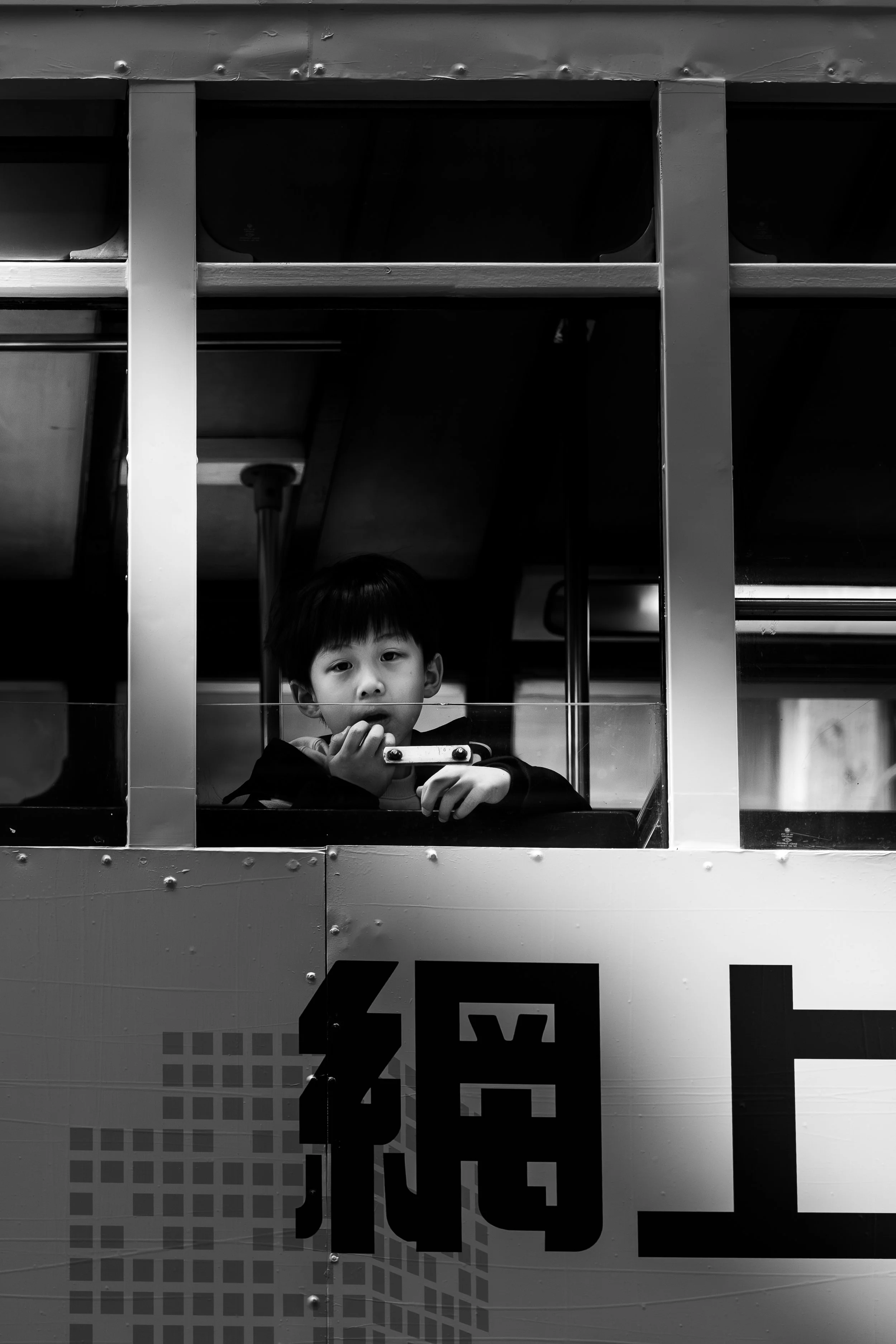 A young boy with dark hair looking through a window on a bus, holding a small object in his hand.