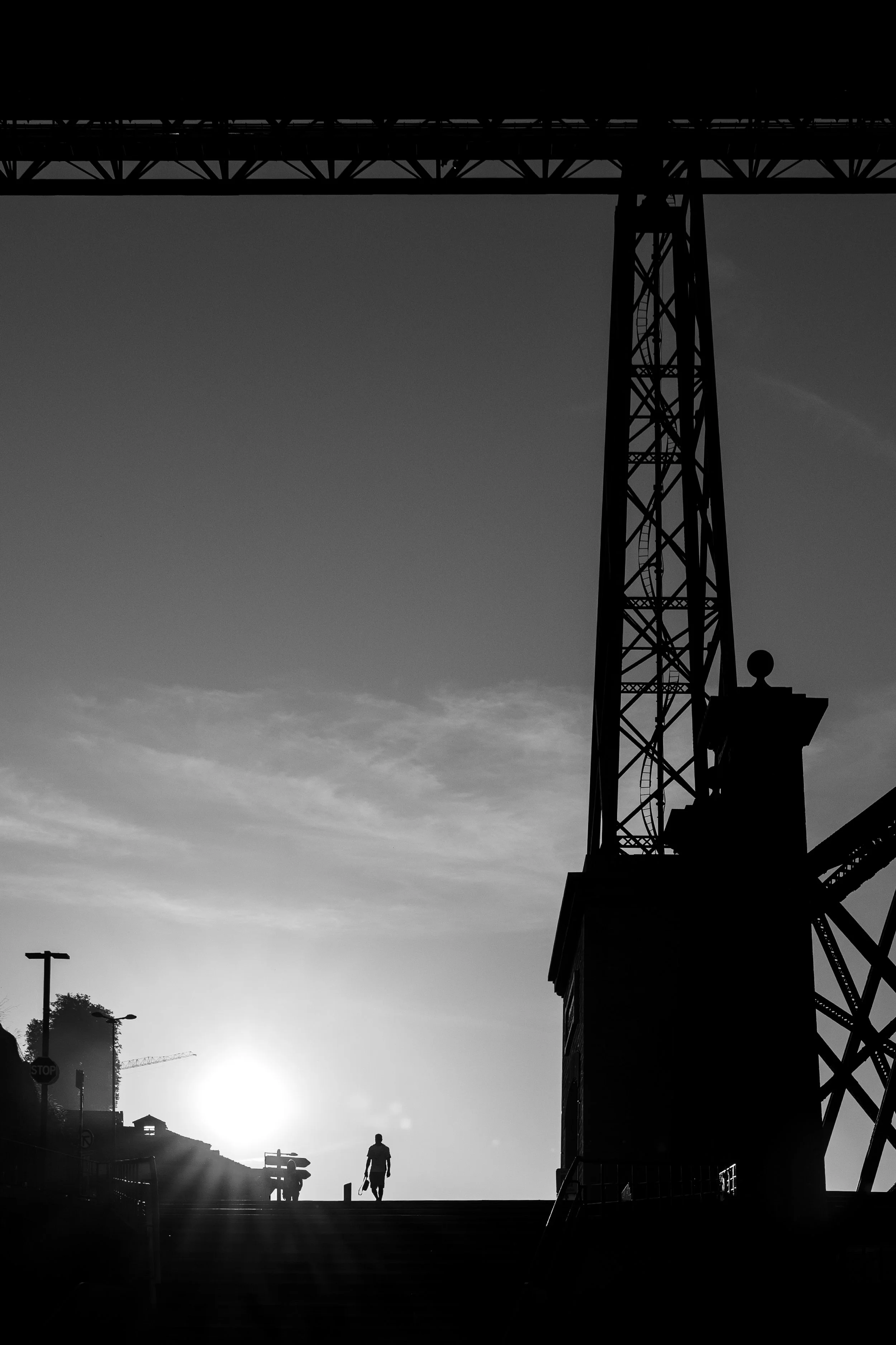 Silhouetted people walking up stairs outdoors during sunset or sunrise, with a large industrial tower and utility poles in the background.