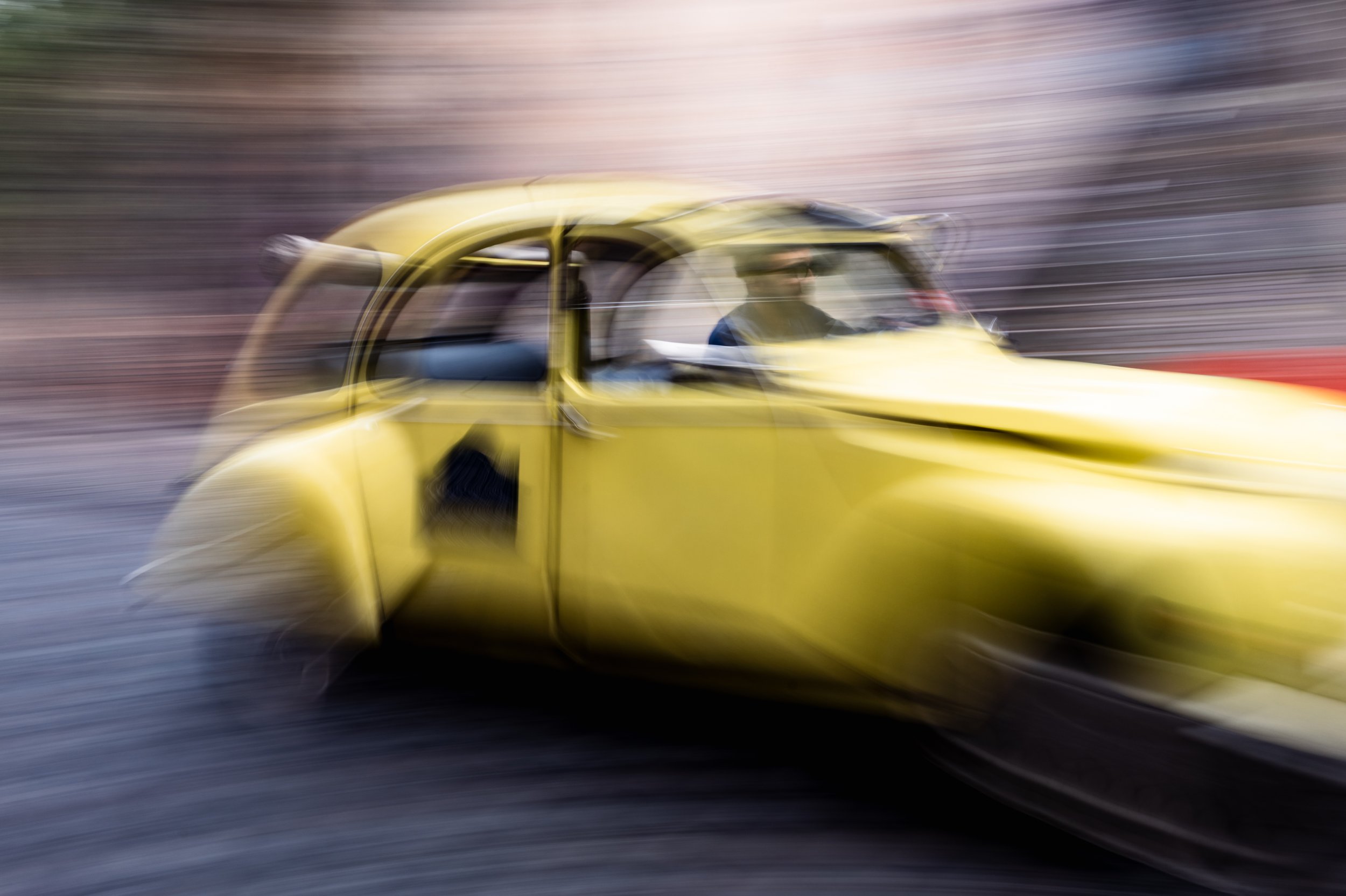 A yellow car speeding down a racetrack, captured with motion blur to show high speed and movement.