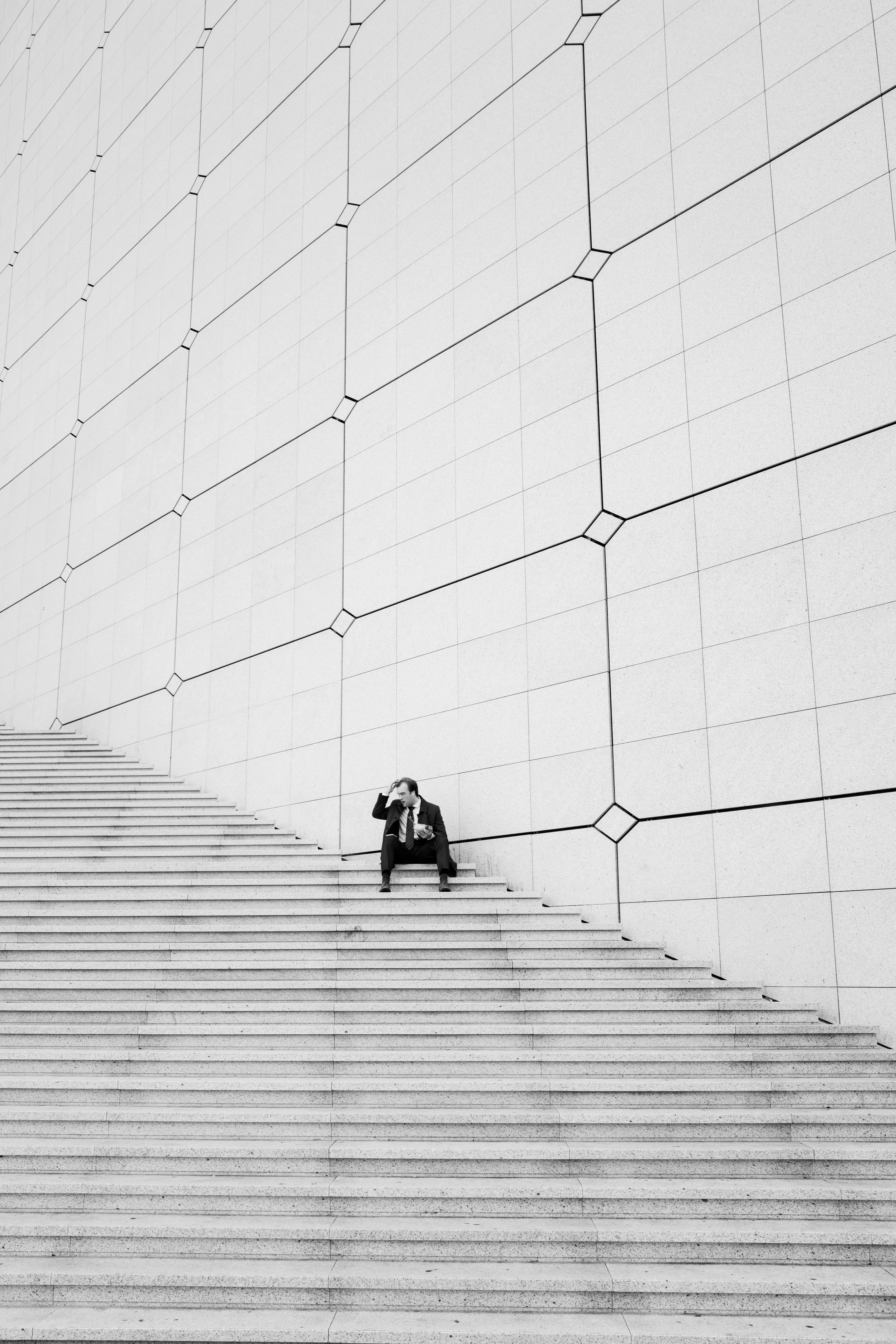 A man in a suit sitting on stairs in front of a modern geometric wall.