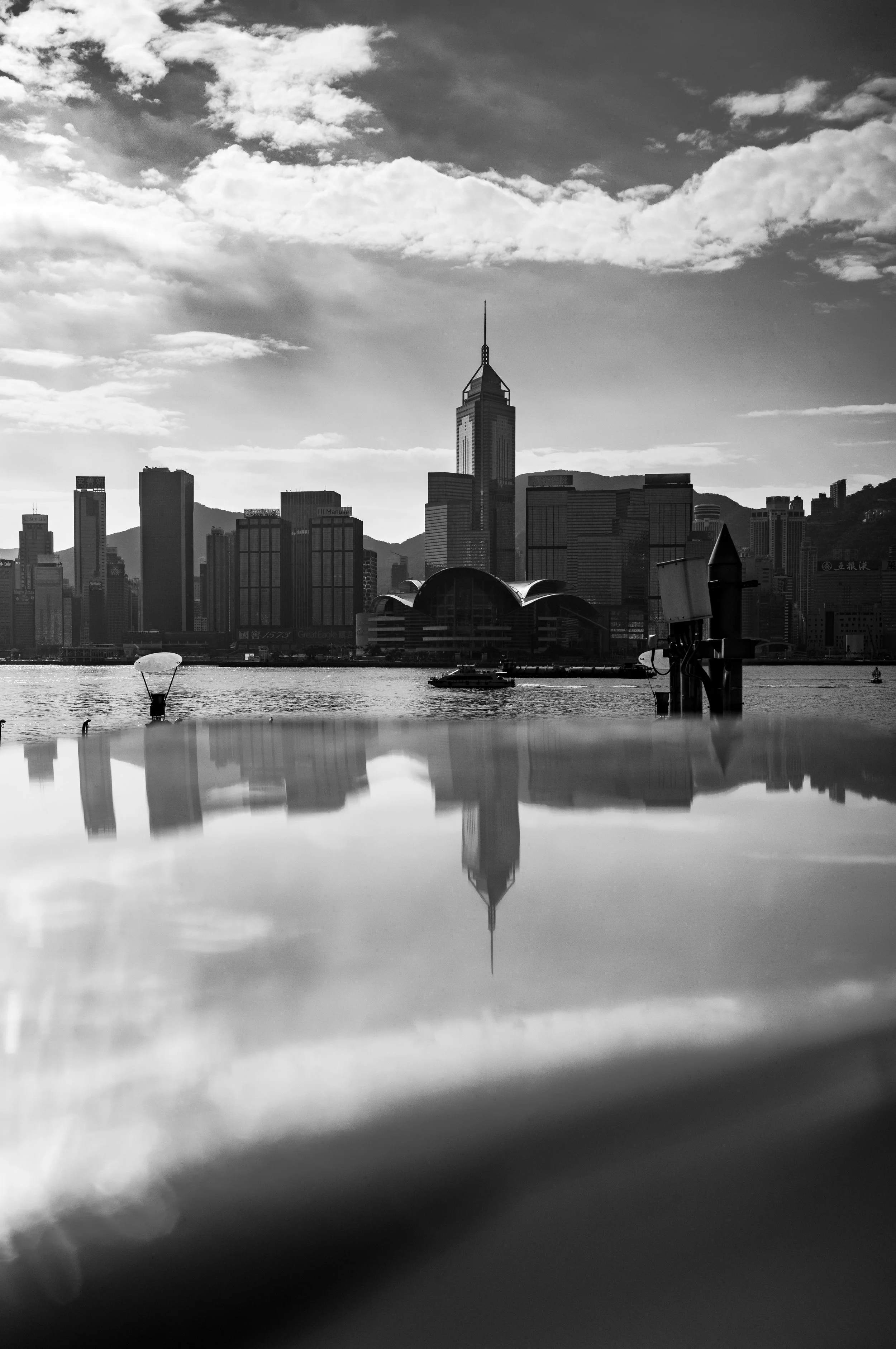 A city skyline with tall buildings reflected in a body of water, with a partly cloudy sky overhead.