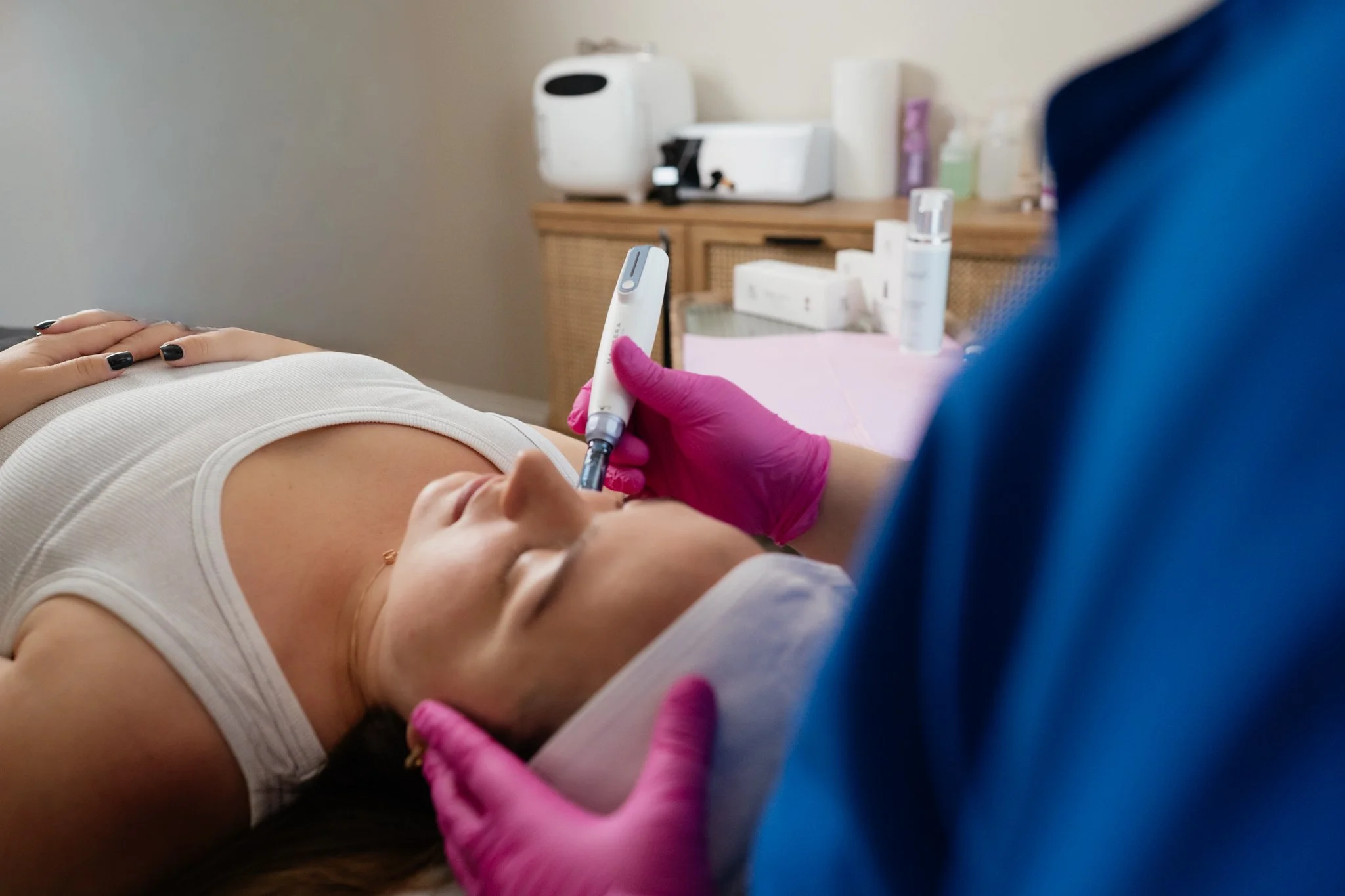 A woman lying on a medical examination table during a medical test, with a healthcare professional wearing pink gloves using a device on her abdomen.