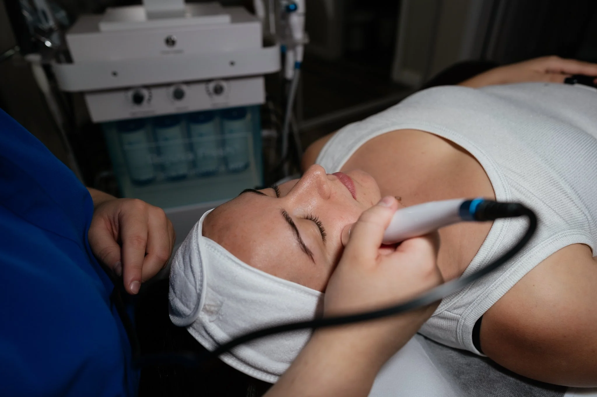 A woman lying down during a medical procedure, with a healthcare professional holding a diagnostic device near her face, in a clinical setting.