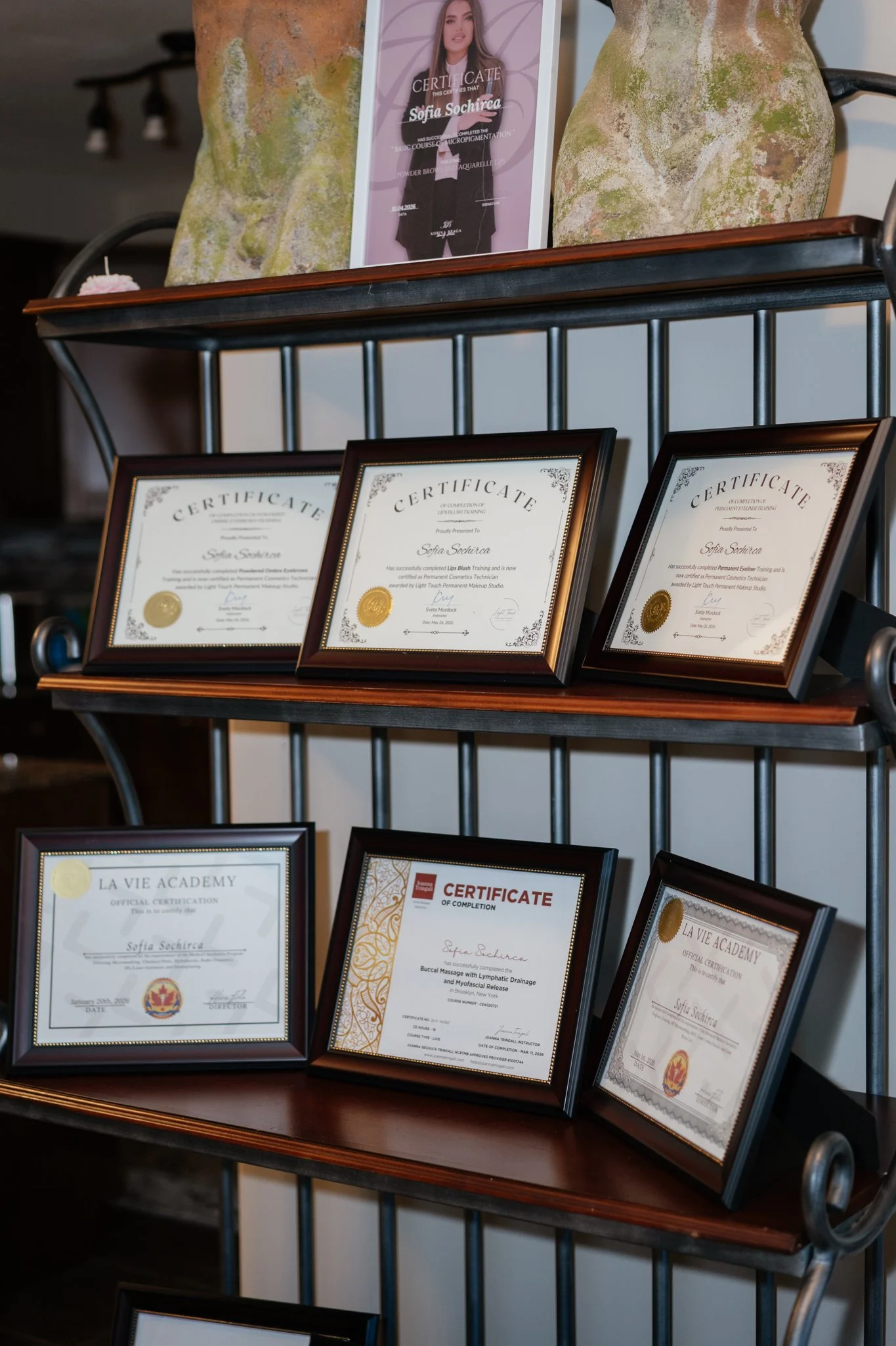 Display shelf with multiple framed certificates and awards, including one with a photo of a woman and a certificate of completion, in a professional setting.