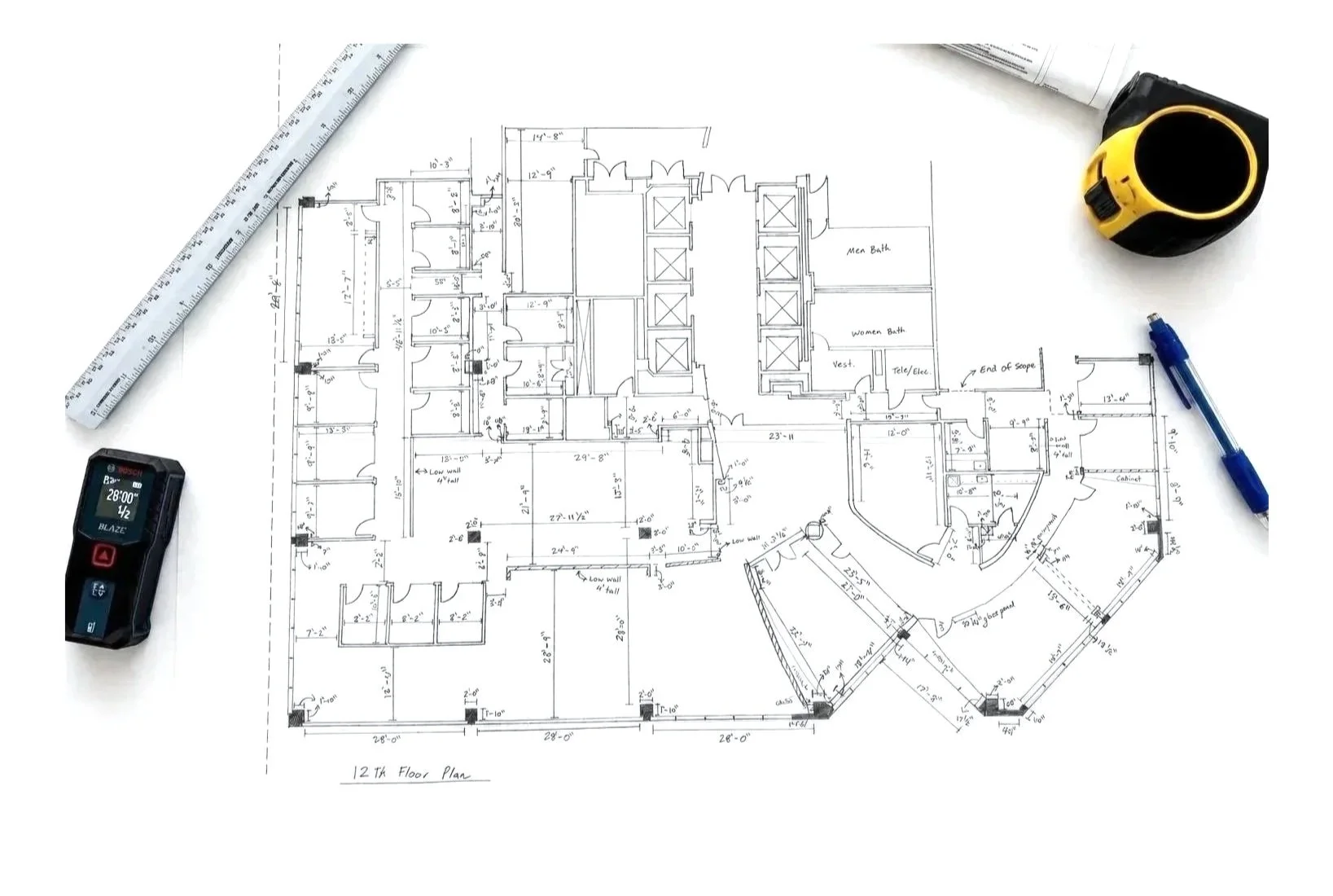 Architectural floor plan drawing on white paper with measurement tools and a digital recorder on white surface.