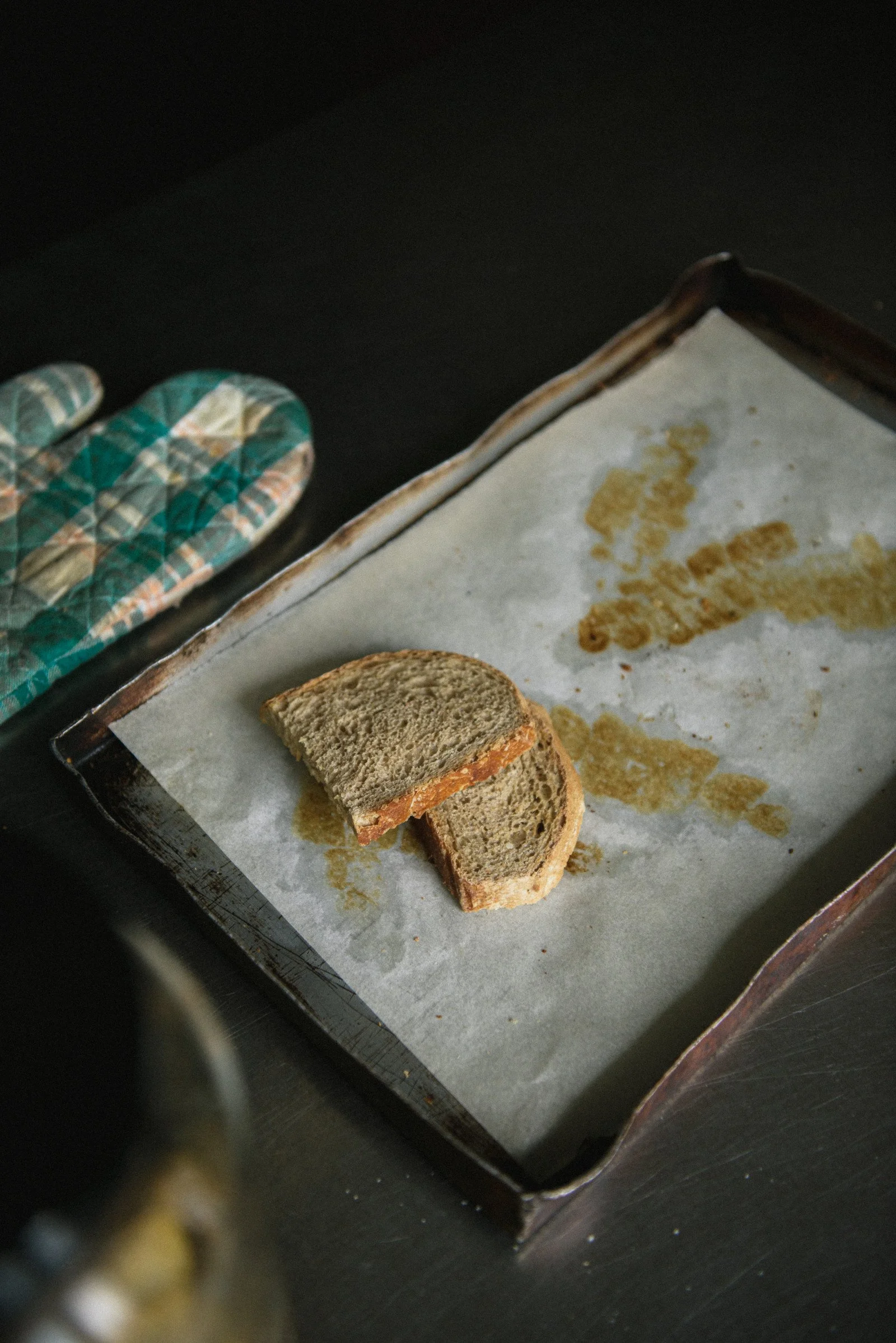 Sliced bread on a parchment-lined baking tray beside a quilted oven mitt