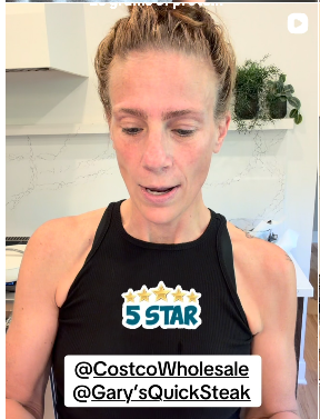 A woman with light skin and reddish-brown hair tied back, wearing a black athletic top, looking down slightly, with a sticker reading '5 STAR' on her chest. There are tags @CostcoWholesale and @Gary'sQuickSteak at the bottom of the image, indoor background with a plant.