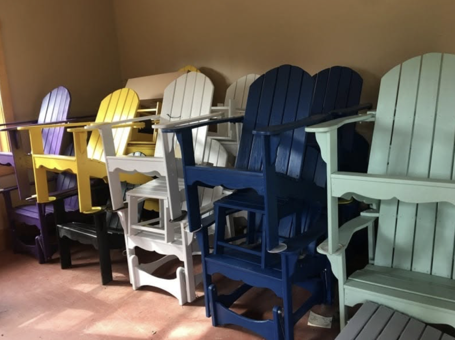 Stacked colorful wooden Adirondack chairs in yellow, white, blue, and mint green.