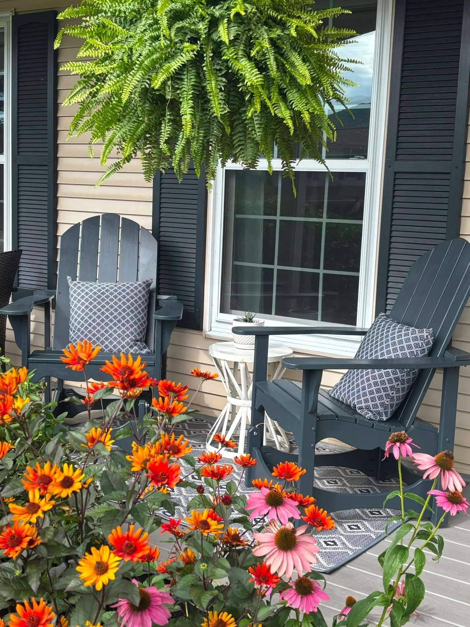 2 gray Adirondack glider chairs on a front porch with orange and pink flowers in foreground