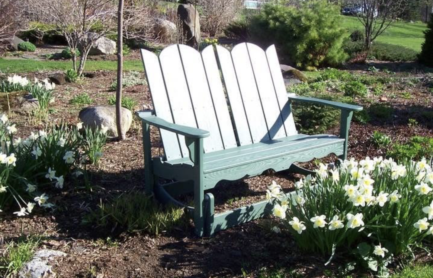 A light blue Adirondack-style bench in a garden with blooming white and yellow flowers.