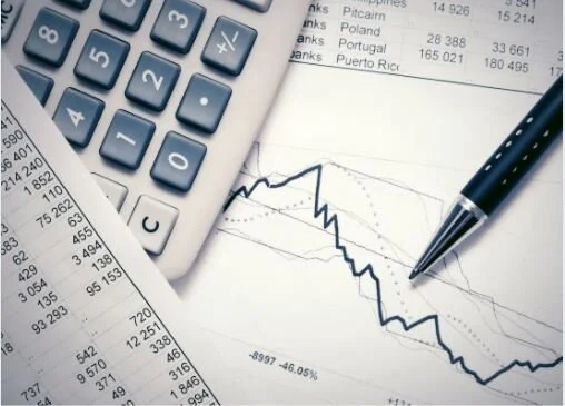 Calculator, pen, printed financial charts, and spreadsheets on a desk.