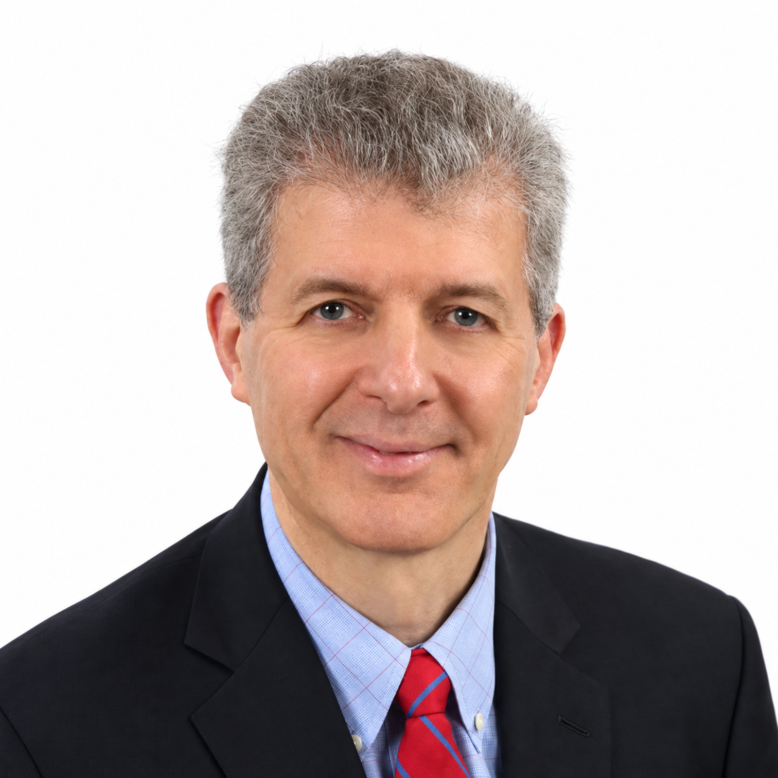 Headshot of a middle-aged man with gray hair wearing a black suit, light blue shirt, and red tie, smiling against a white background.