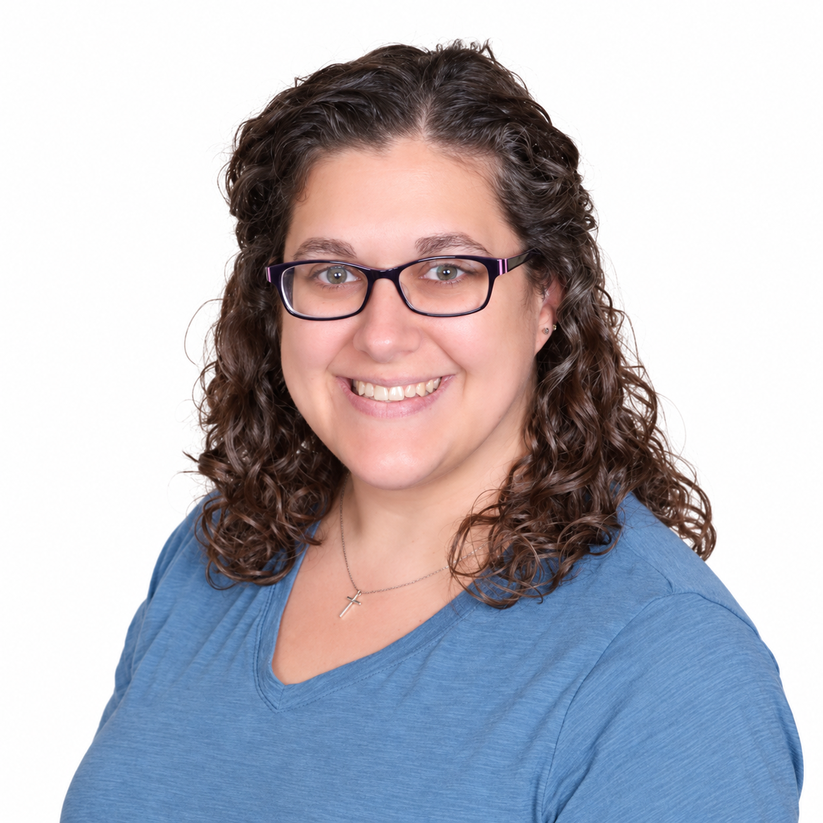 A woman with curly brown hair wearing glasses and a blue top, smiling against a plain white background.