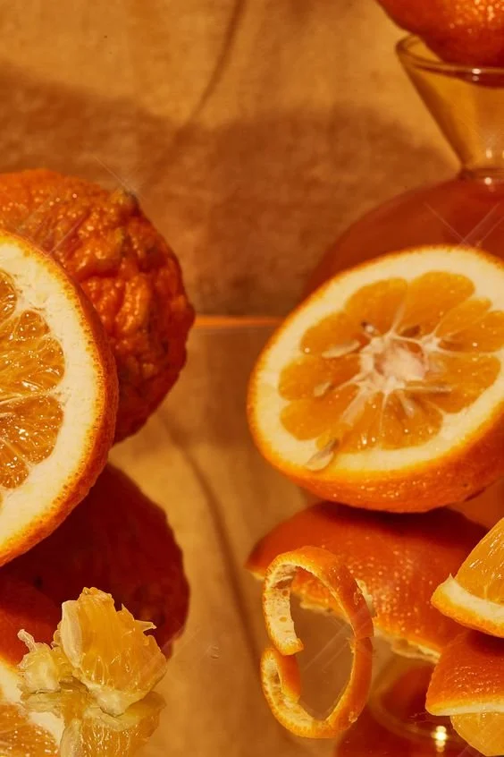 Close-up of sliced oranges and a whole orange on a wooden surface, with a small glass of orange peel.