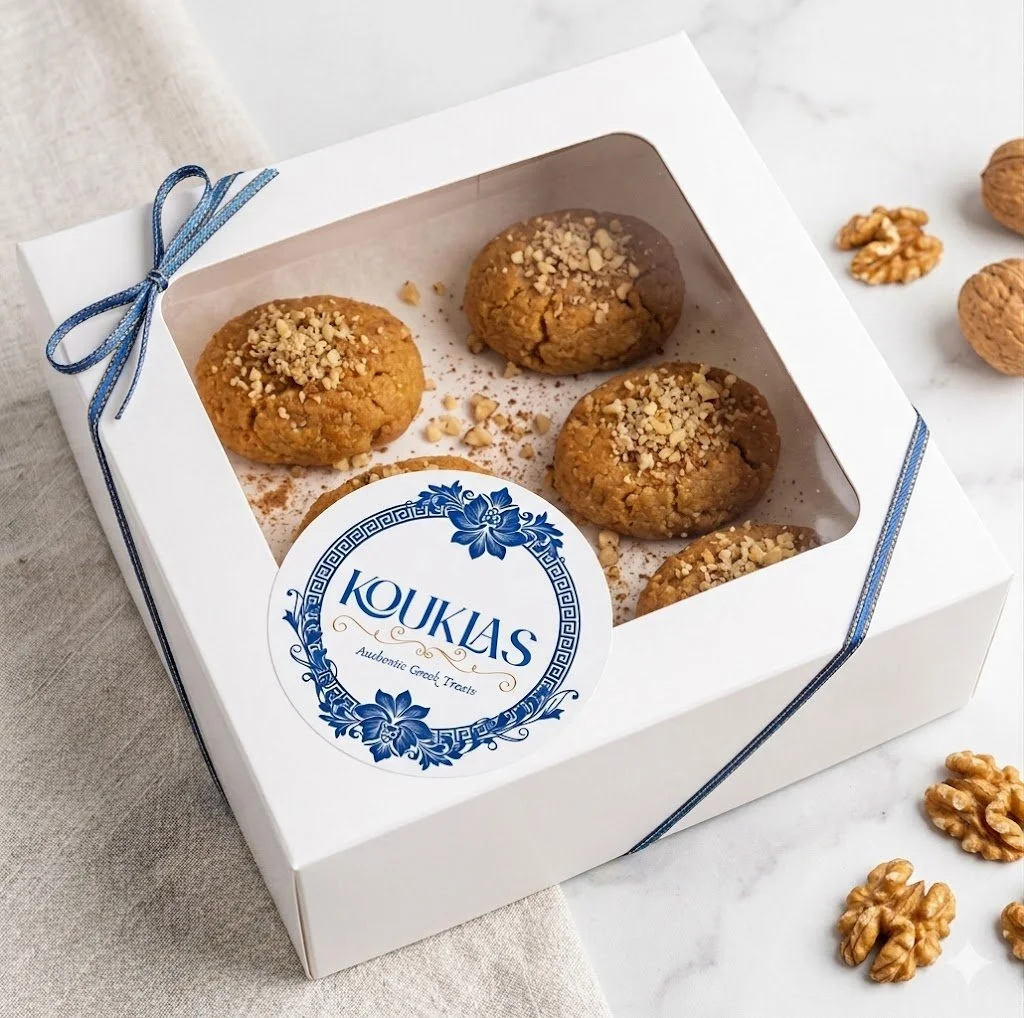 A white box of four cookies topped with chopped nuts, labeled 'KOUKIAS Audobic Crozet Treats', with walnuts around the box on a marble surface.