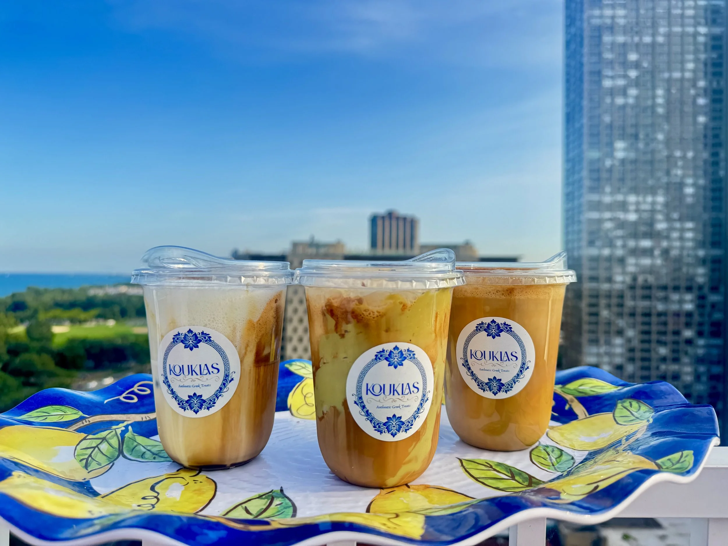 Three cups of Greek frozen yogurt on a colorful tablecloth with a cityscape and blue sky in the background.