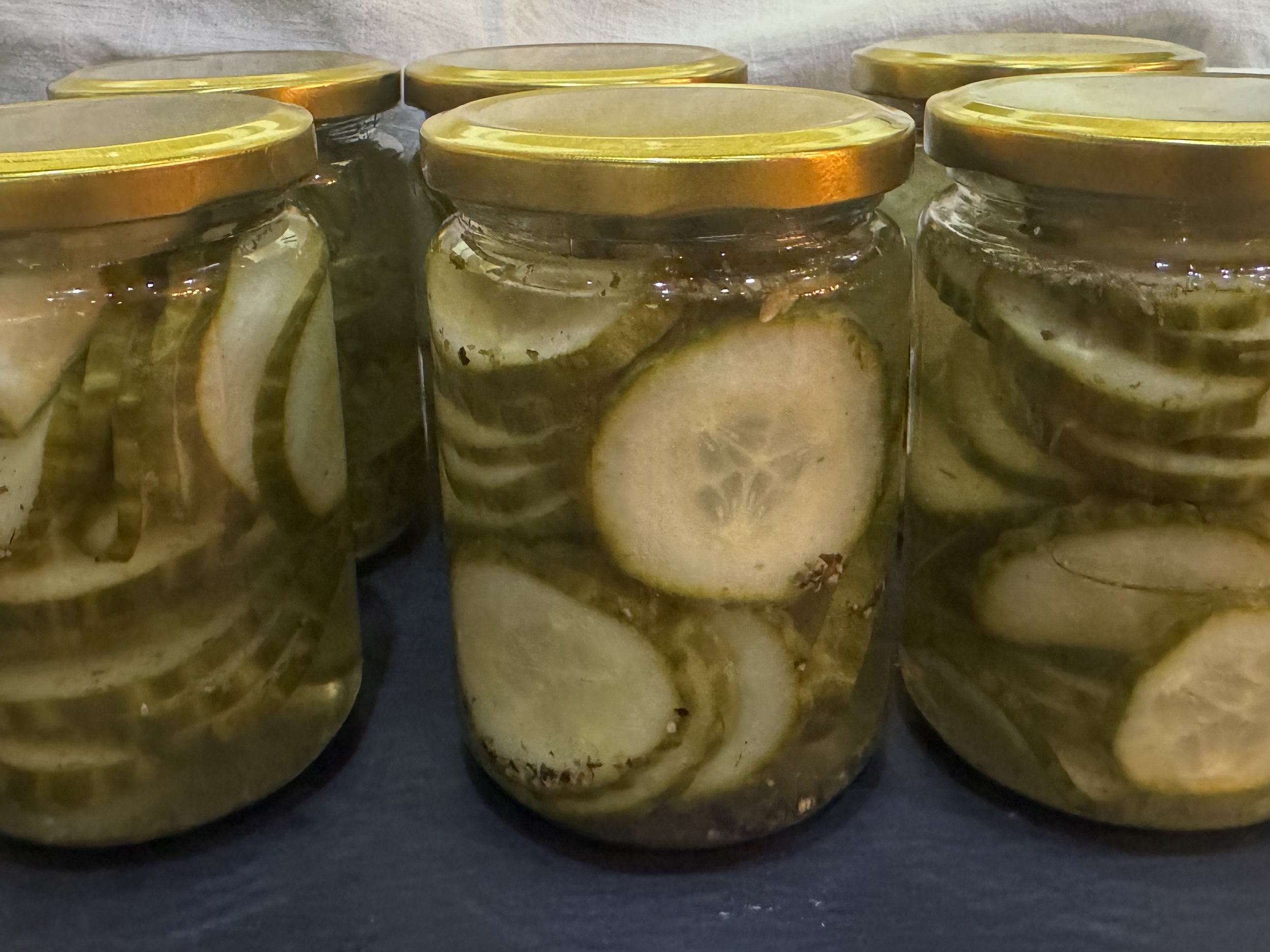 Close-up of multiple glass jars with sealed golden lids, containing a transparent substance with floating chunks, placed on a dark surface.
