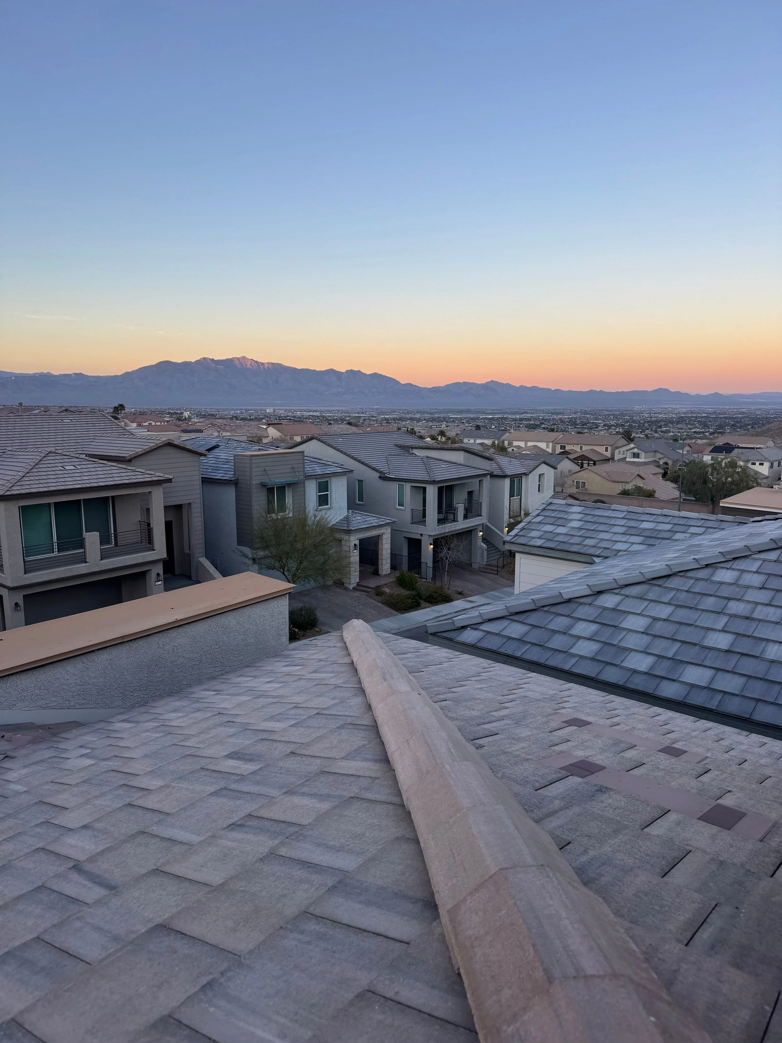 Residential rooftops with mountains in the distance during sunset.
