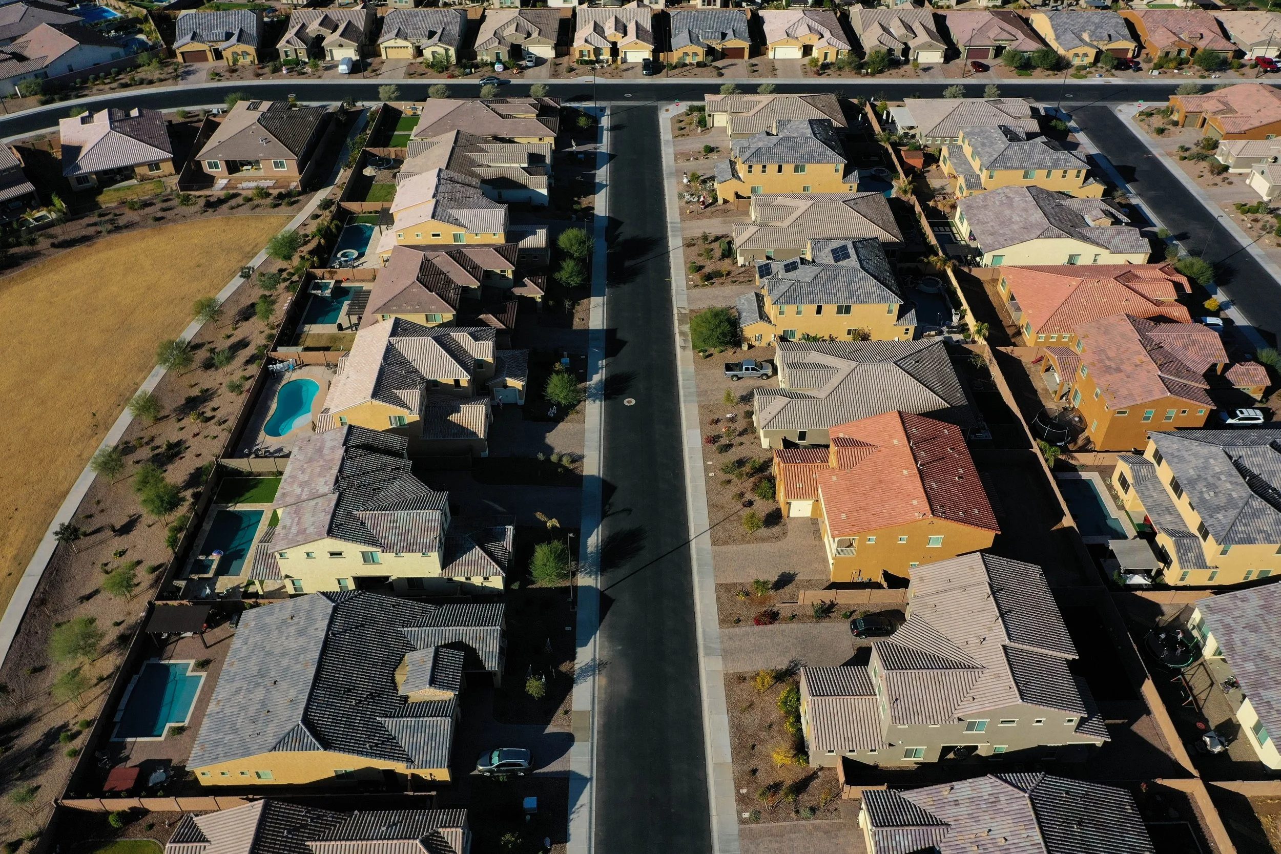 Aerial view of a neighborhood with multicolored houses featuring different roof styles, some with pools and front yards, and a street running through the middle.