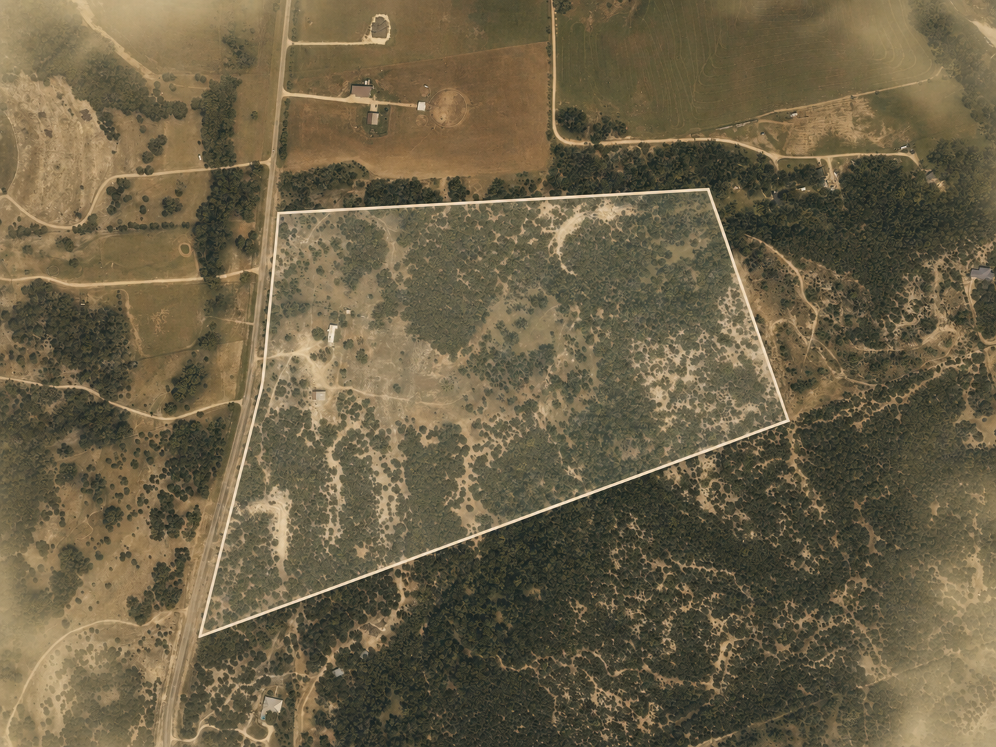 Aerial view of a large property outlined with white border, featuring wooded areas, open fields, and a few structures, with roads and pathways interconnecting the land.