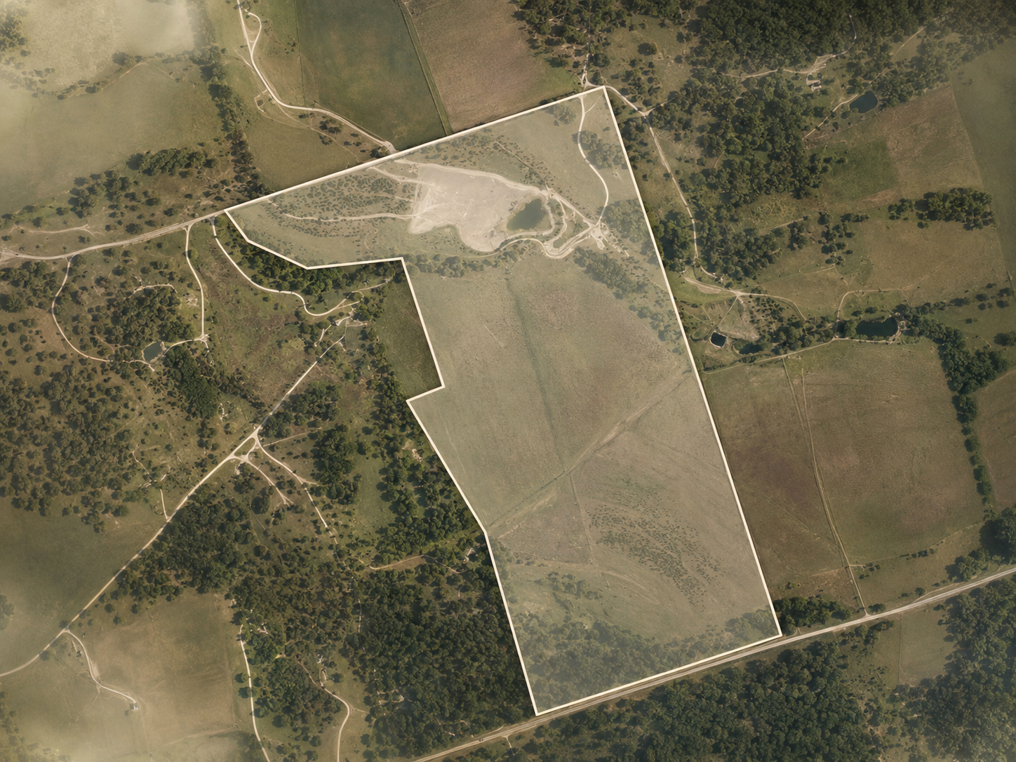 Aerial view of a large rural property outlined in white, featuring fields, wooded areas, ponds, and winding dirt roads.