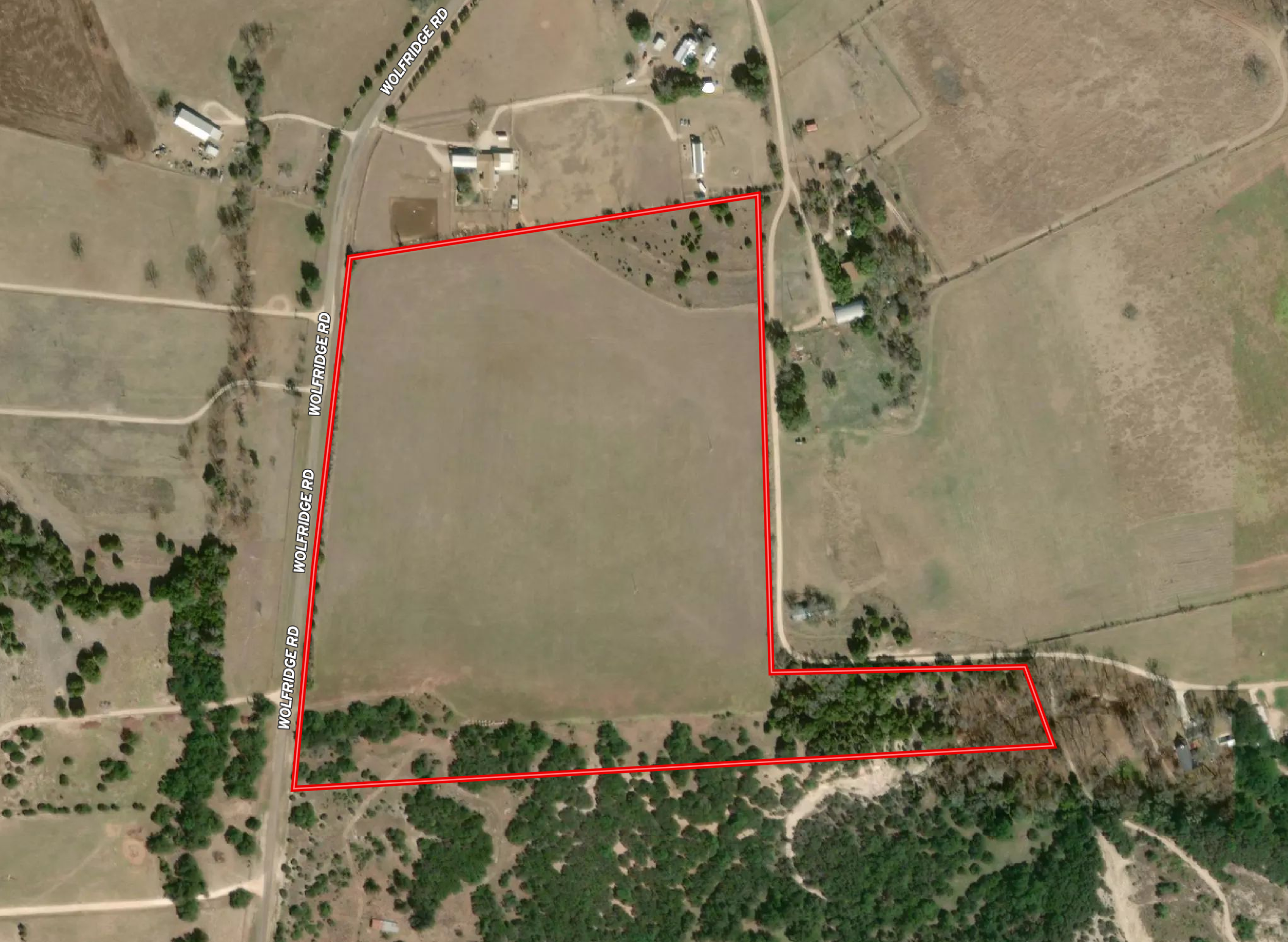 Satellite image showing a rural area with fields, trees, and buildings. A red outline marks a specific property boundary, and a road labeled 'Wolf Ridge Rd' runs along the left side of the image.