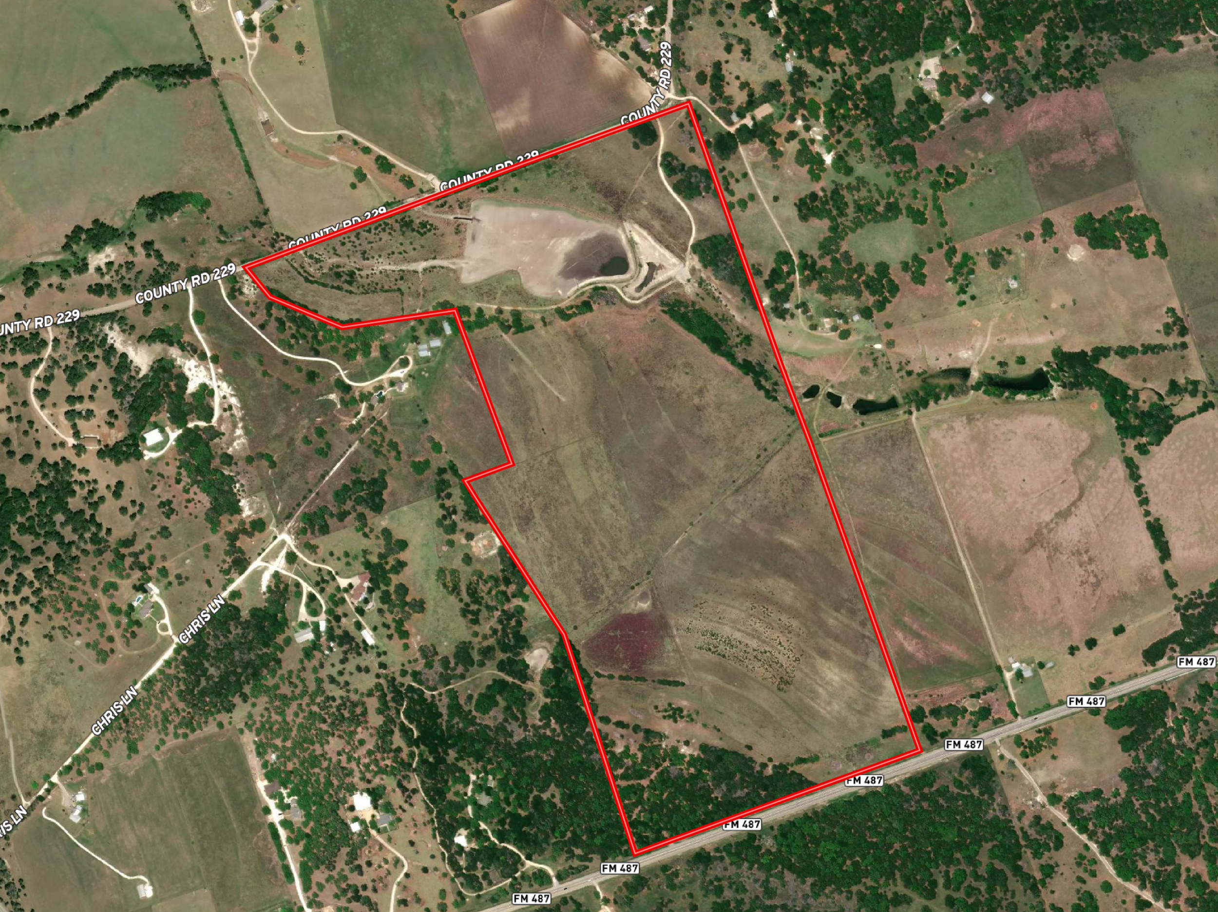 Satellite view of rural area with roads, trees, a pond, and a property outlined in red line.