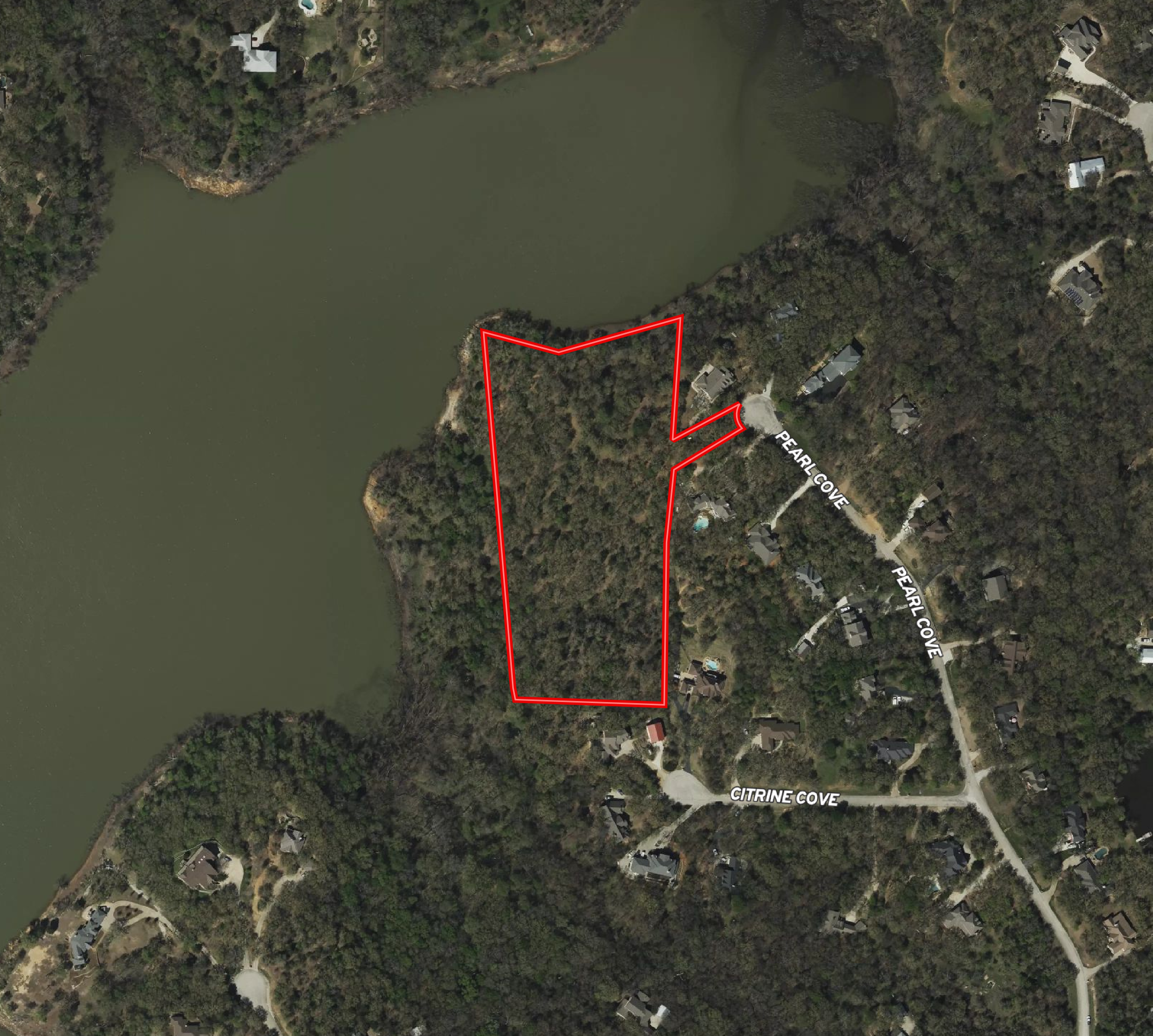Aerial view of a lakeside residential area with houses, trees, and roads. A section of land is outlined in red, with street names 'PEARL COVE' and 'CITRINE COVE' visible.