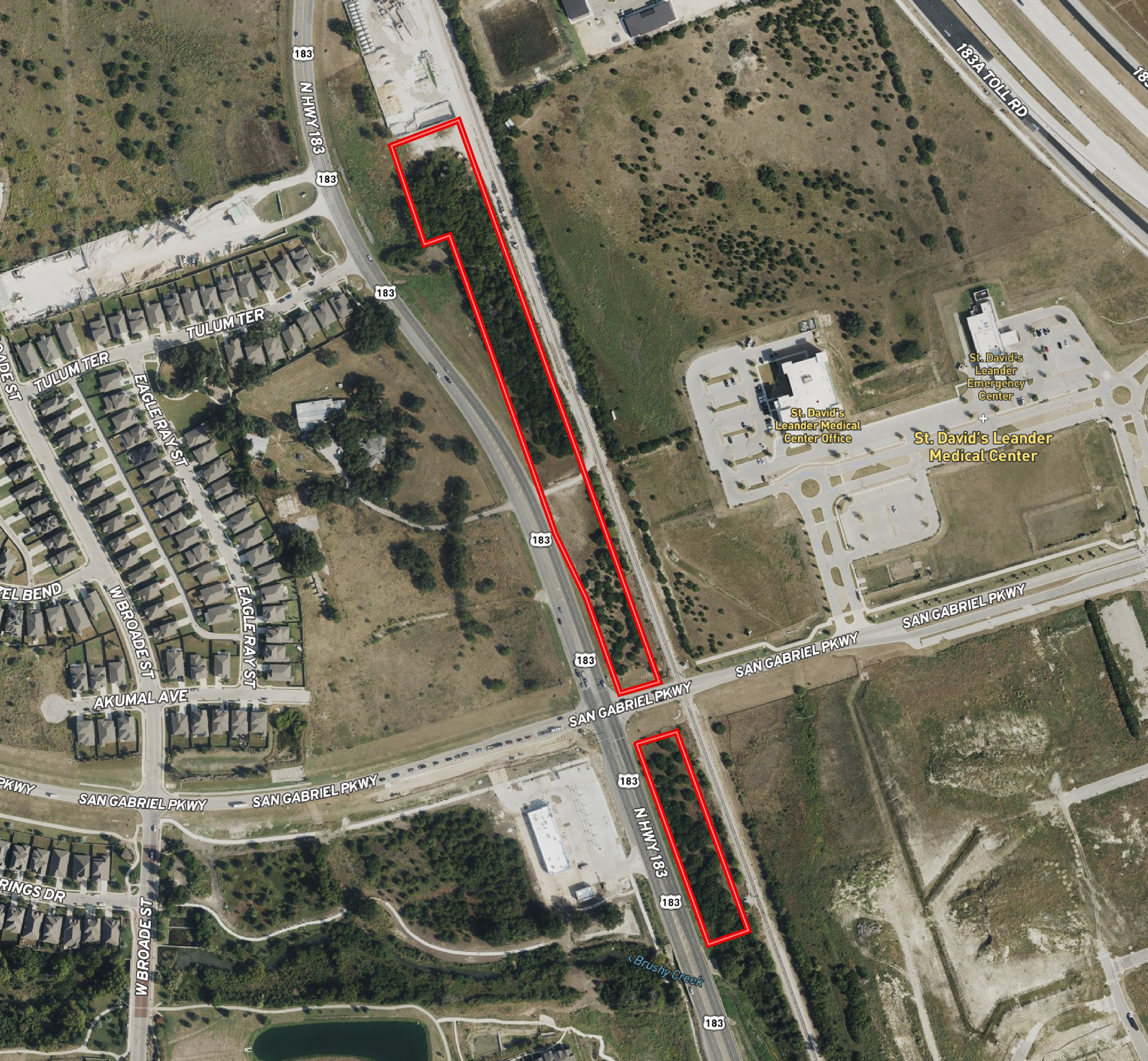 Aerial view of a section of a city showing streets, residential houses, a medical center, parking lots, and a green space enclosed by a red outline along Highway 183.